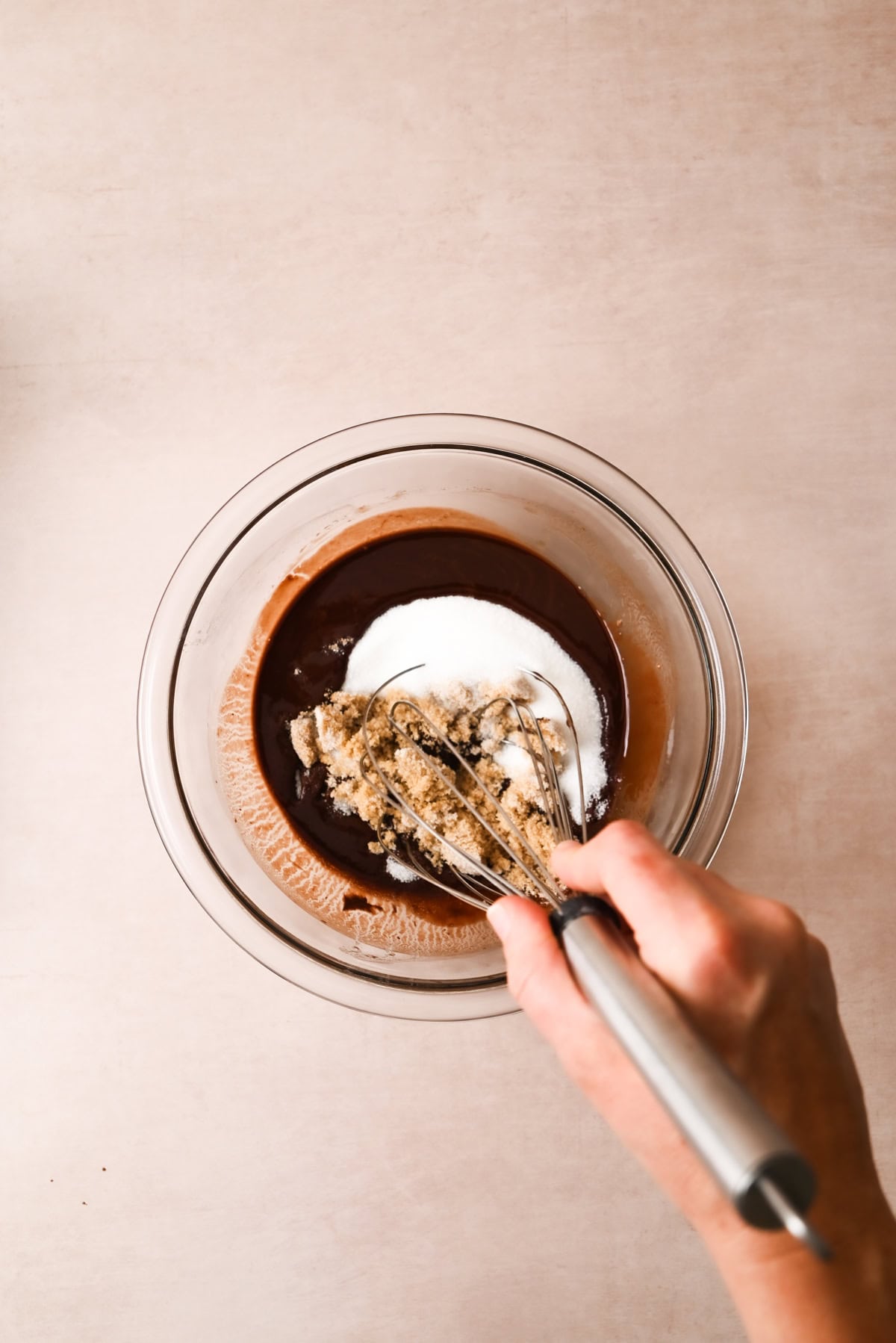 A hand whisking white and brown sugar into a bowl of melted chocolate mixture on a light-colored surface, preparing rich Small-Batch Brownies.
