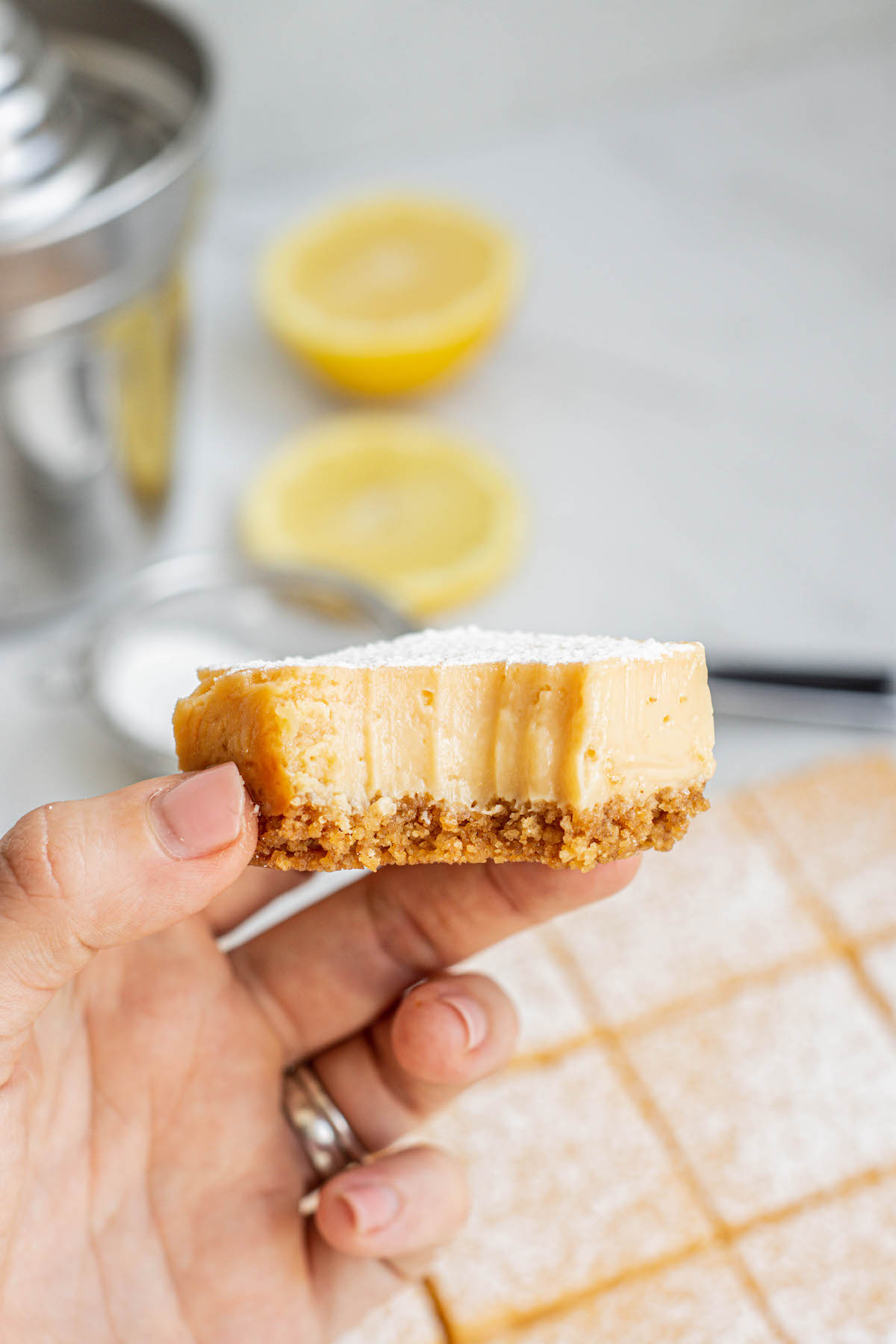 a hand holding a piece of lemon bar with bite missing.