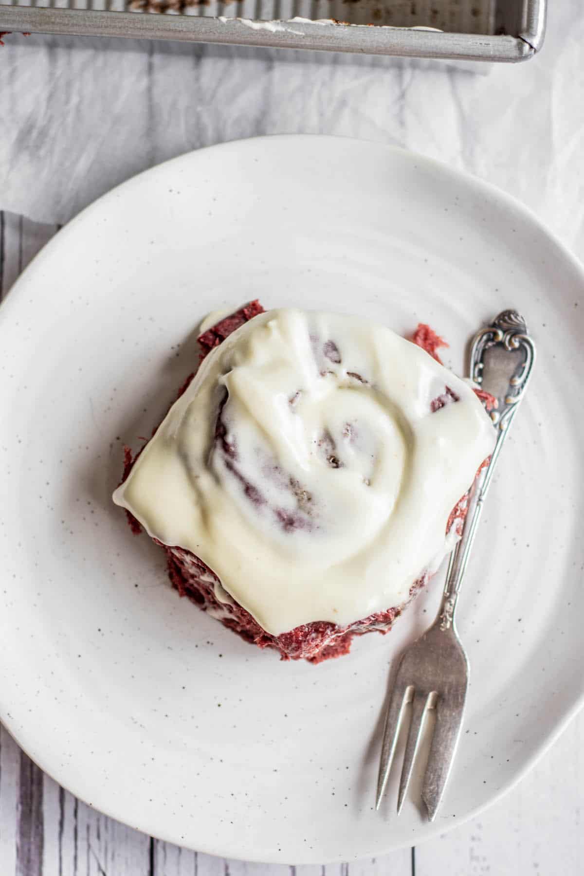 birds eye  view of a red velvet cinnamon roll recipe with cream cheese frosting on a plate.