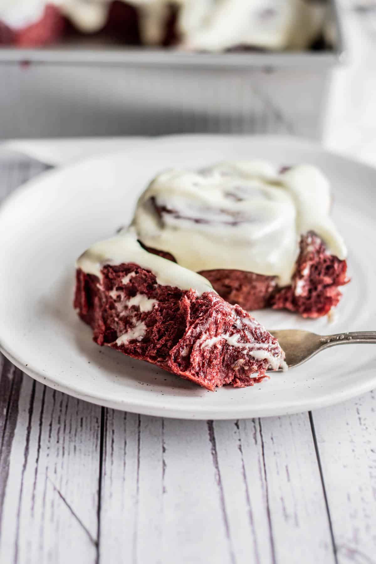 A red velvet cinnamon rolls with cream cheese icing on a plate.
