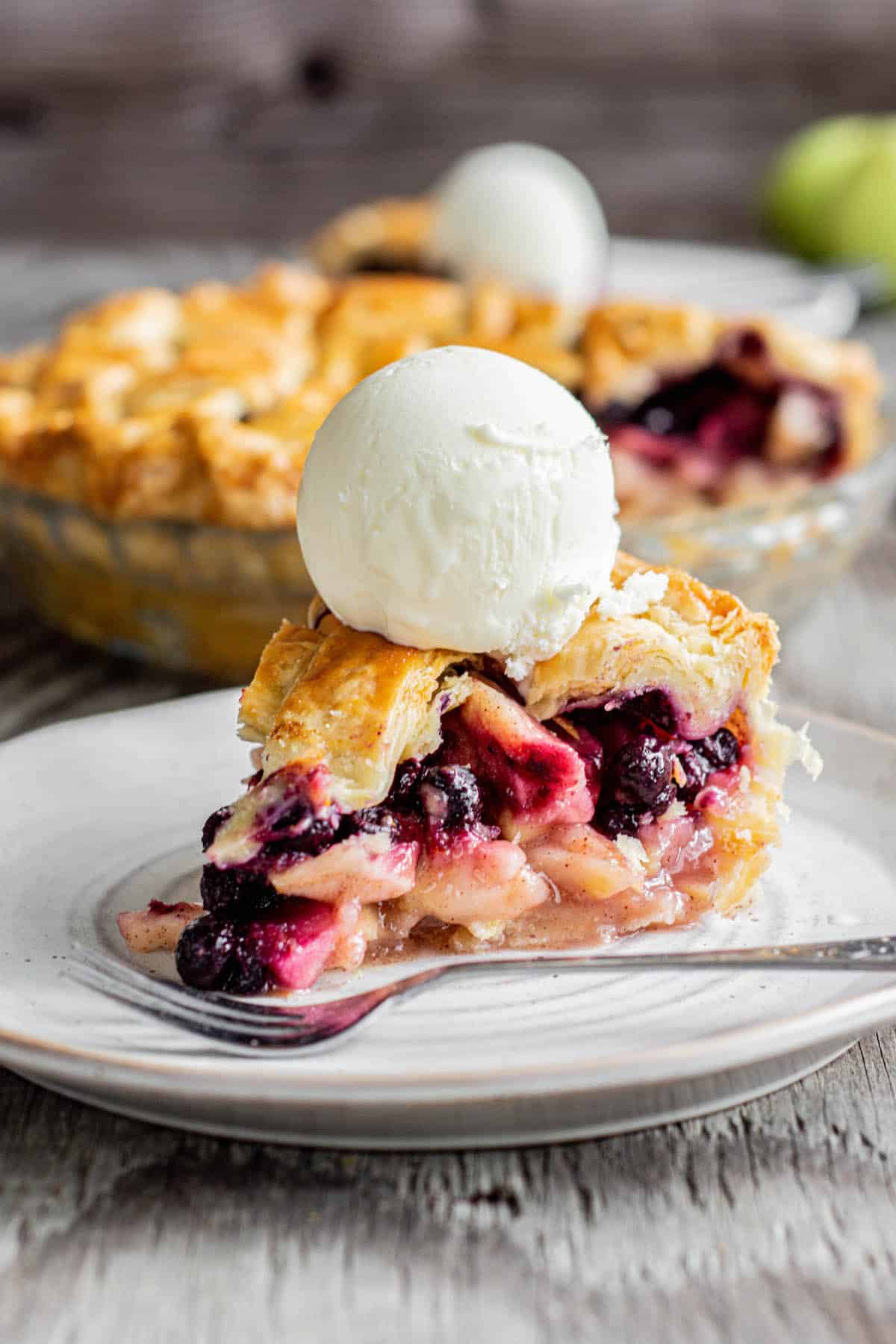 blueberry apple pie on white plate with scoop of ice cream.