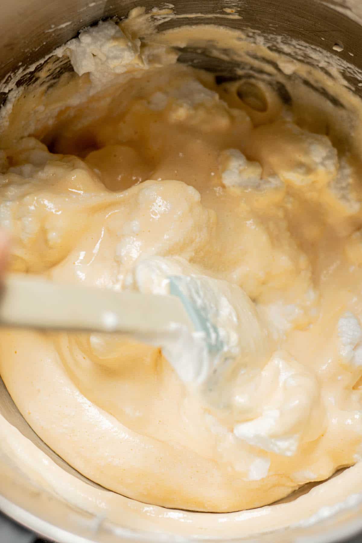 egg whites being folded into batter with blue spatula.