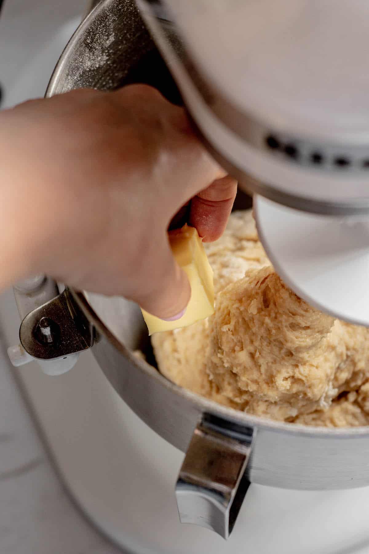 hand adding butter to mixer.