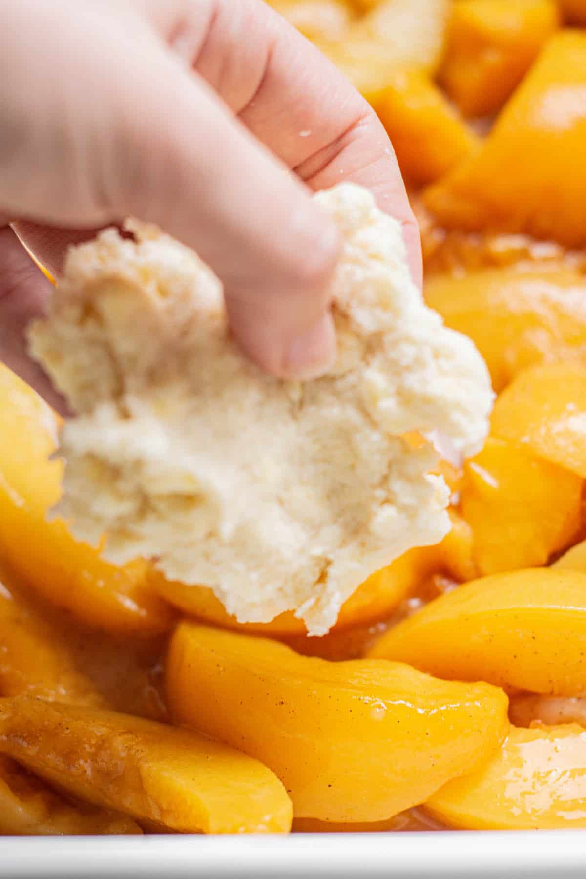 a hand laying a biscuit on peaches.