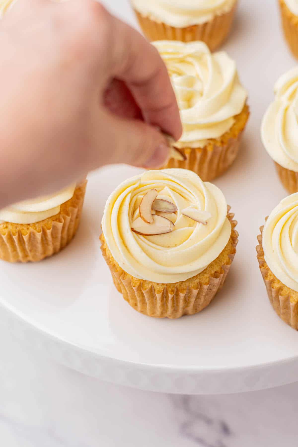 almond cupcakes with hand adding sliced almonds.
