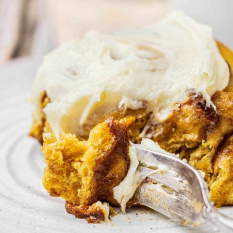 close up of pumpkin cinnamon rolls on a plate with a fork.