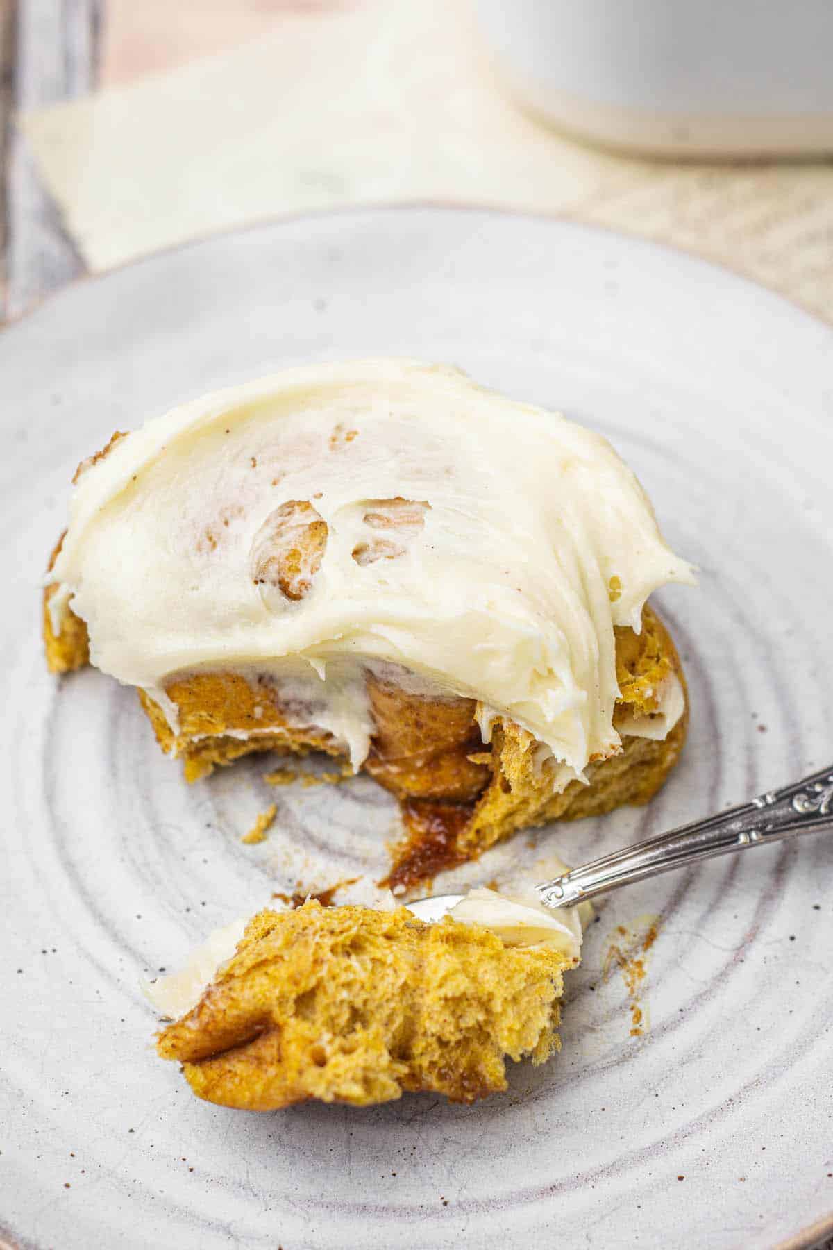 a fork taking a forkful of pumpkin rolls with cream cheese frosting.