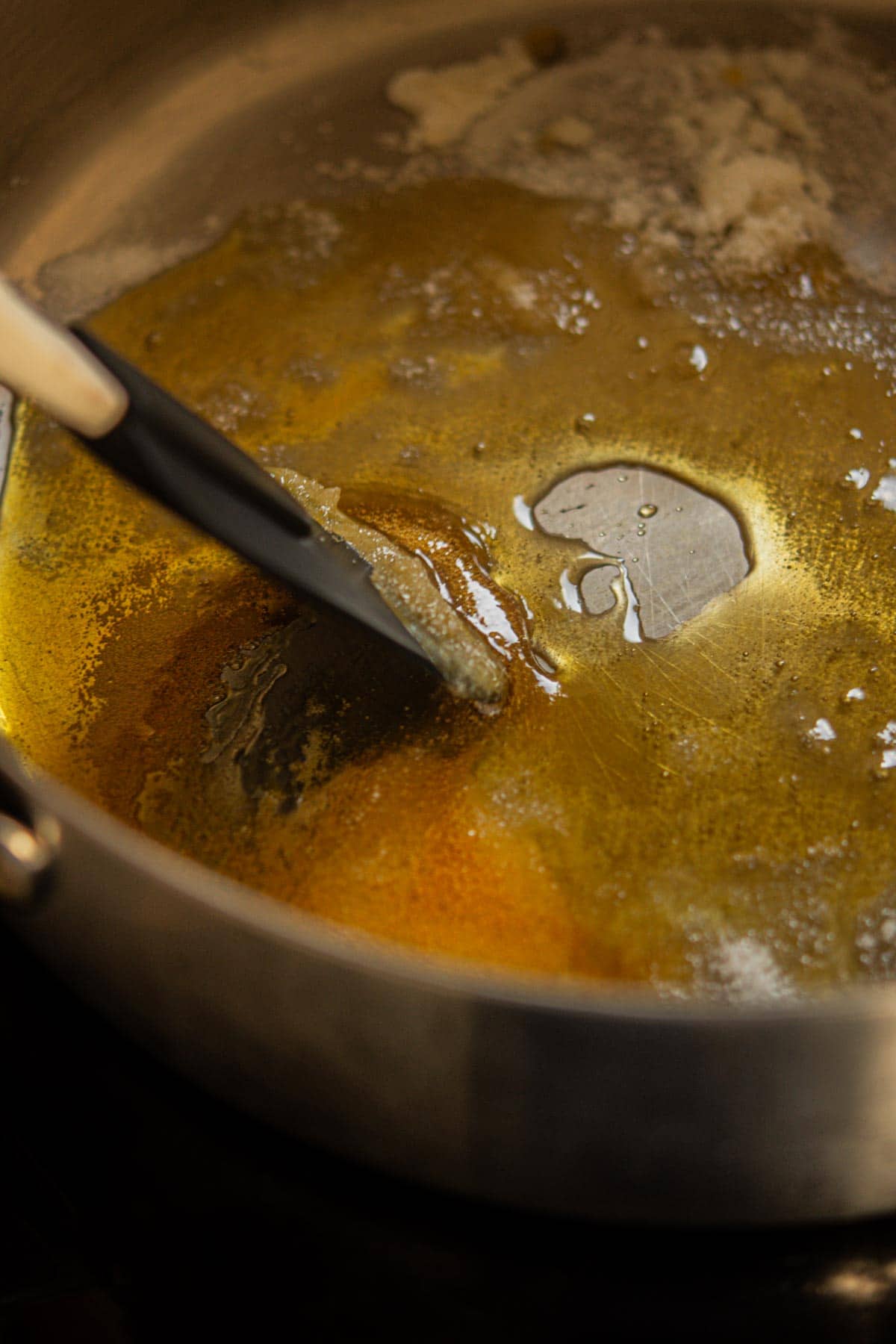 A close-up of a pan with melted brown butter being stirred by a spatula, showing a golden color and foamy texture—the perfect base for rich, nutty Chocolate Chip Pecan Cookies.
