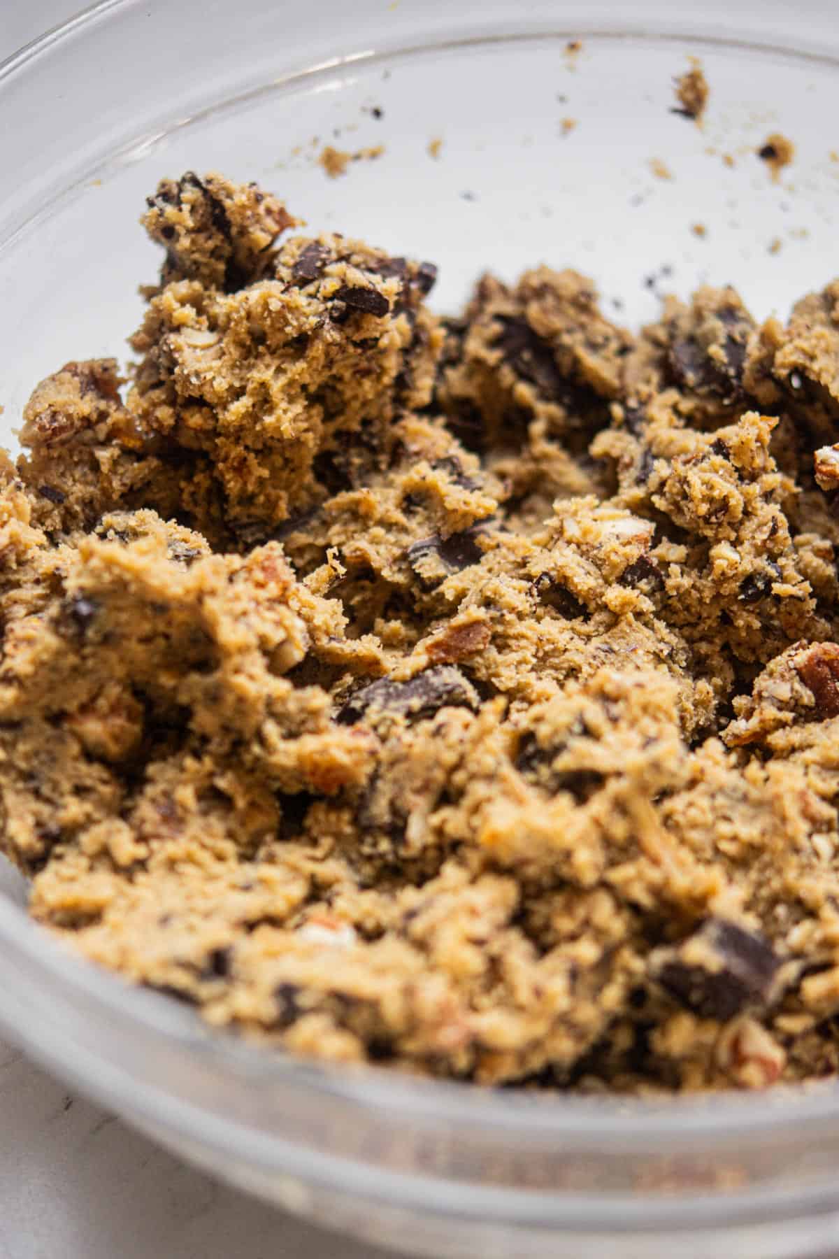 Close-up of raw Chocolate Chip Pecan Cookies dough with visible chocolate chunks and pecans in a clear glass mixing bowl.