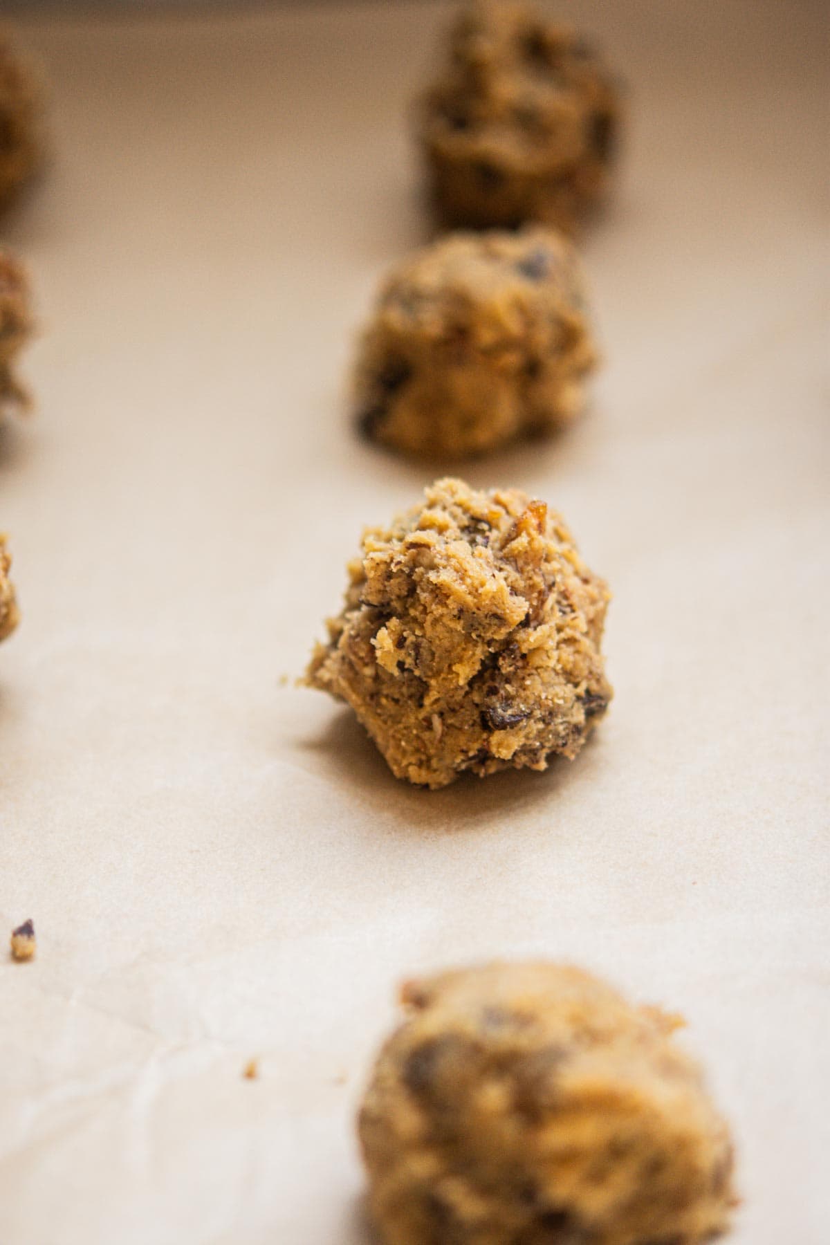 Close-up of several raw Chocolate Chip Pecan Cookies dough balls arranged on a sheet of parchment paper, ready for baking. The focus is on the center cookie dough ball.