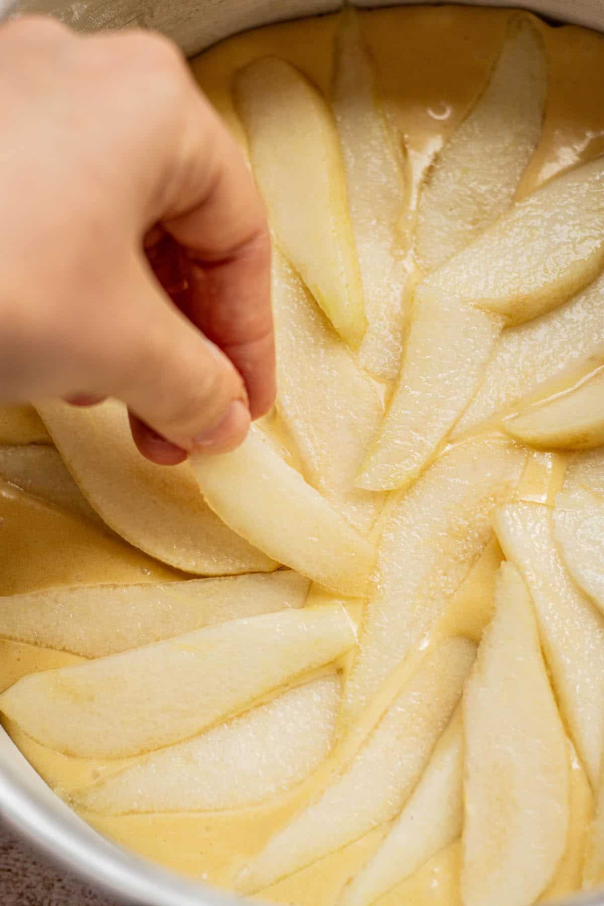 hand arranging pear slices on cake.