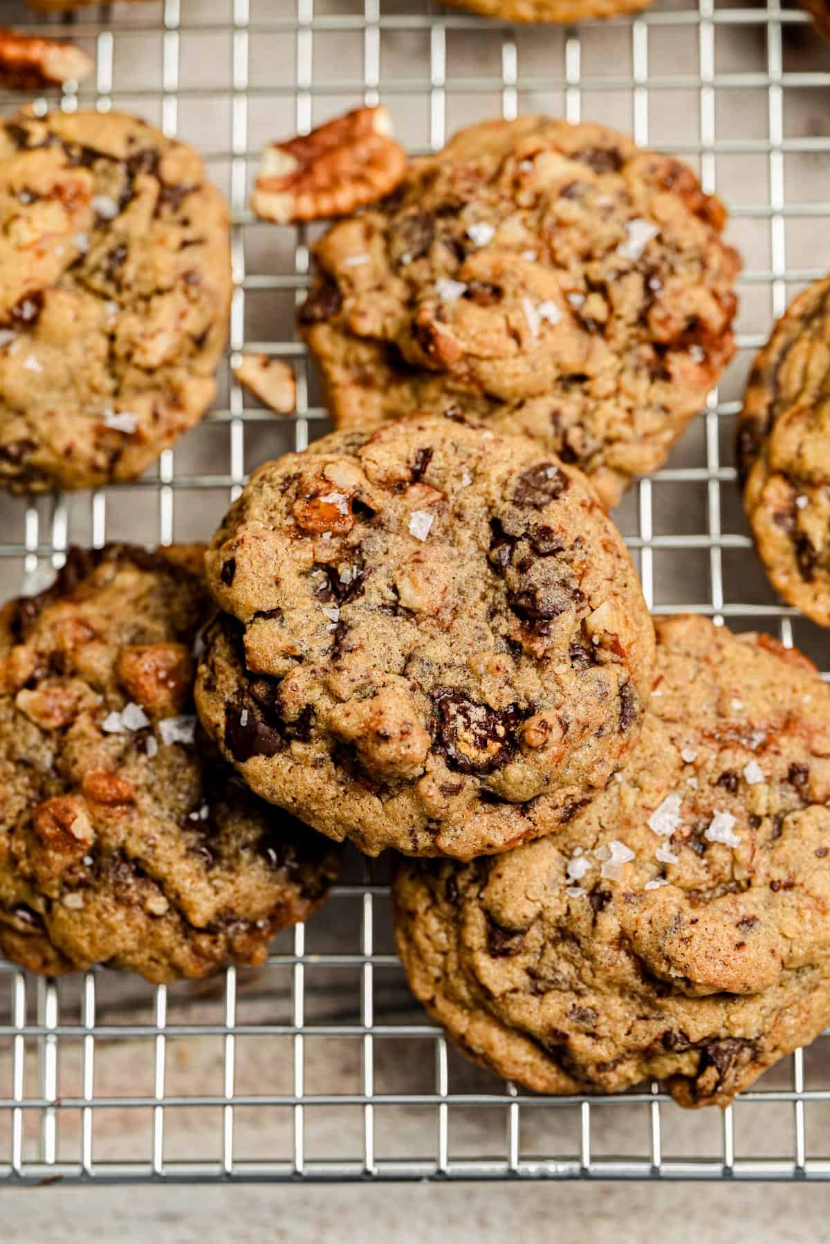 Chocolate Chip Pecan Cookies topped with sea salt flakes cool on a metal wire rack.