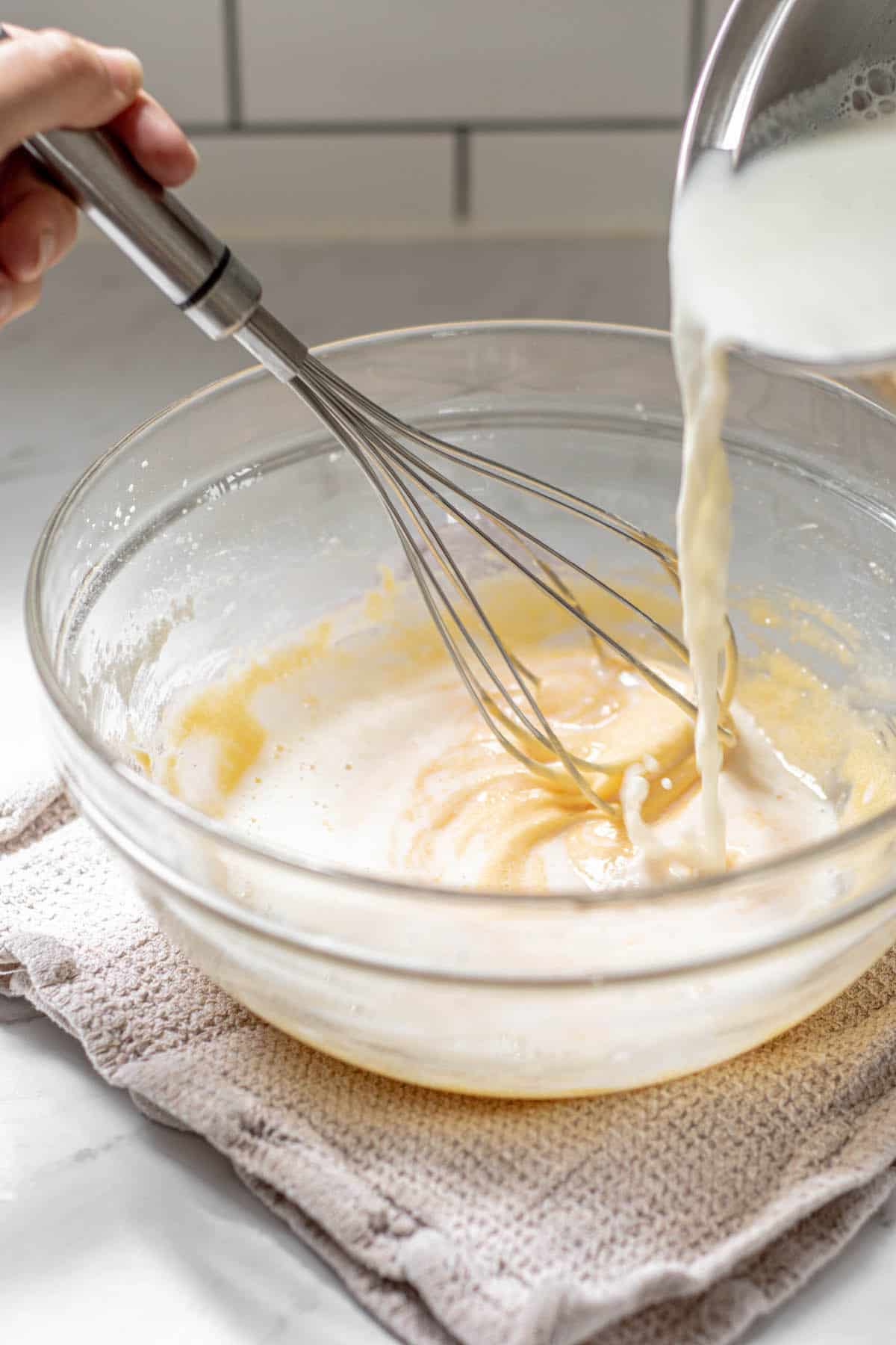 hot milk being poured over whisked egg yolks.