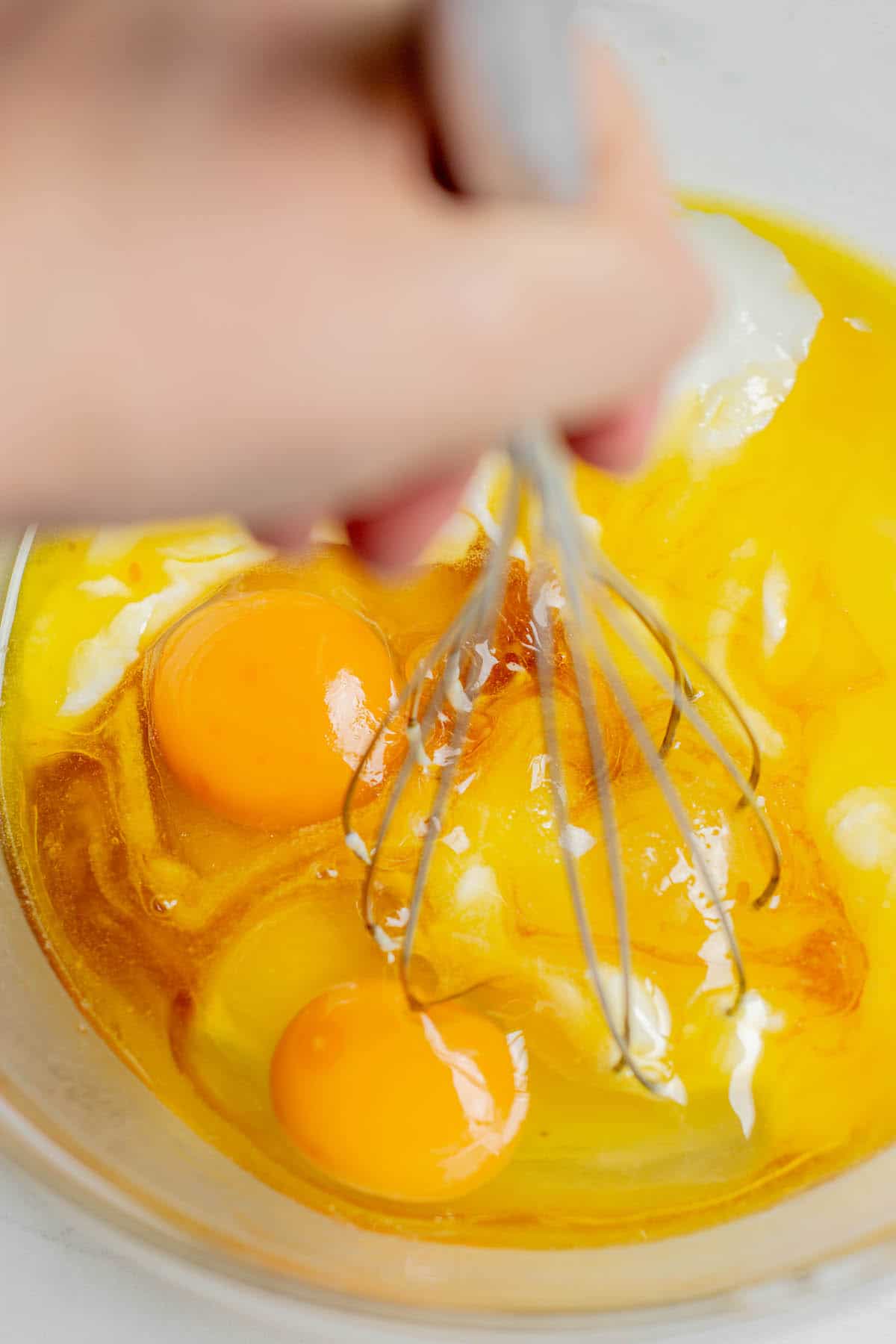 a hand whisking eggs and butter in a glass bowl.