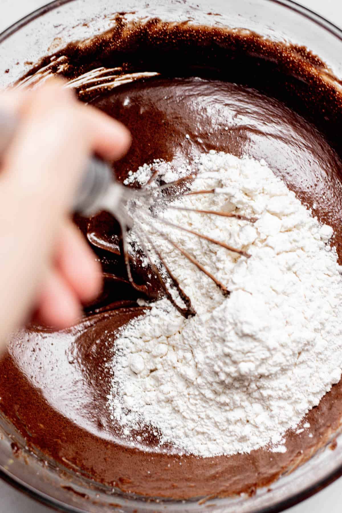 hand whisking flour into chocolate brownie batter.