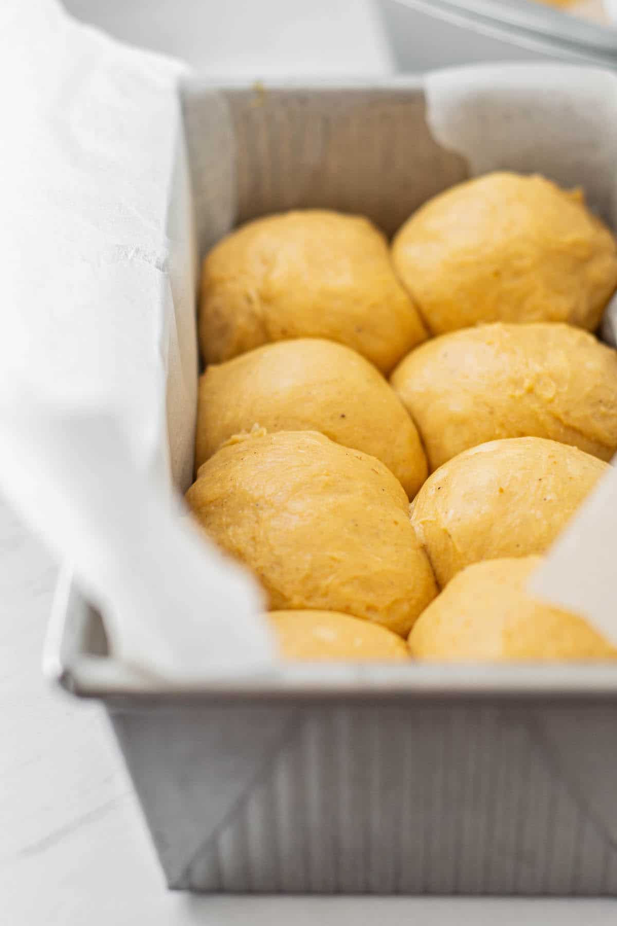 unbaked golden rolls in a metal baking tin.