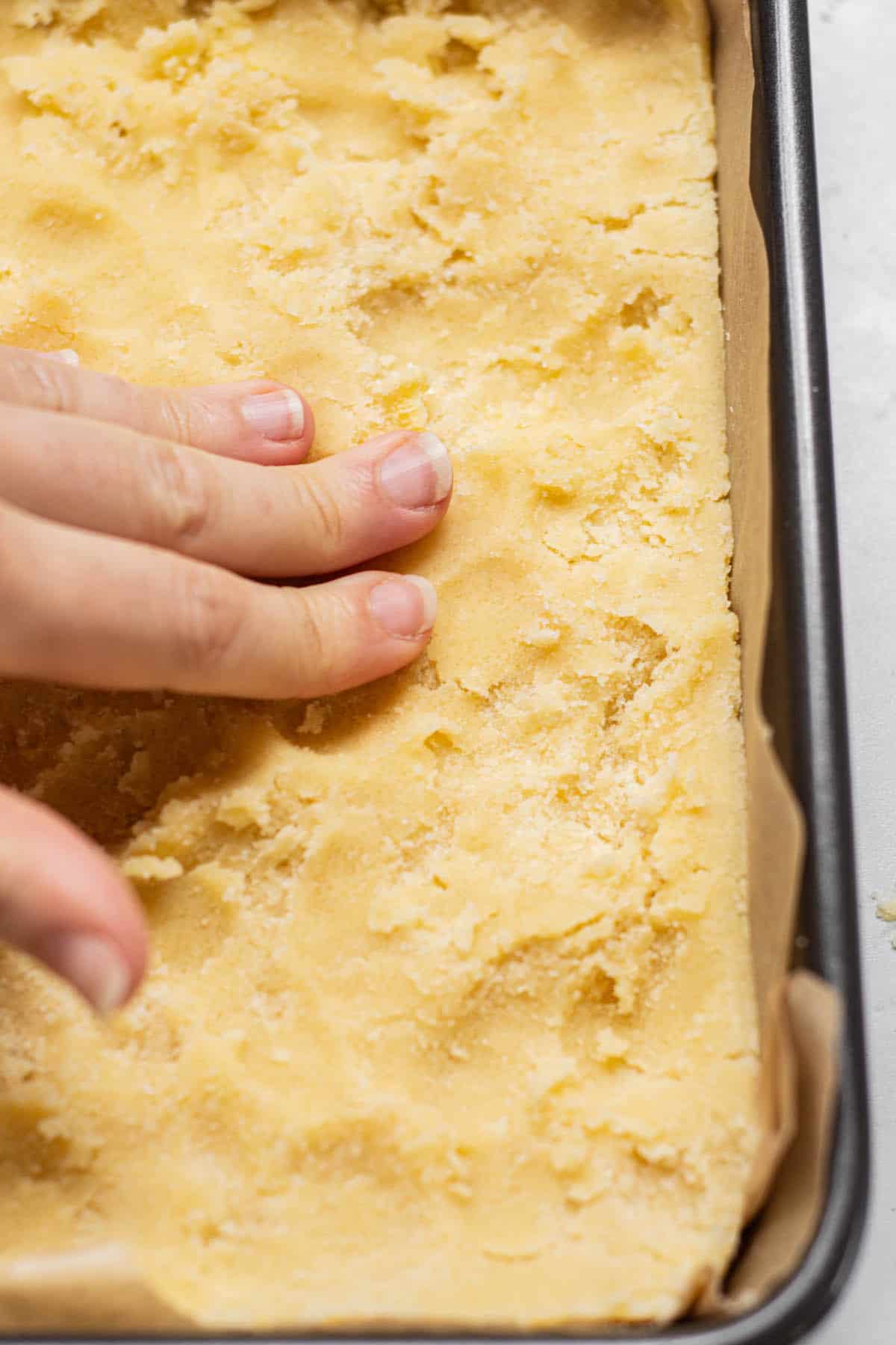 hand pressing boterkoek dough into lined pan.