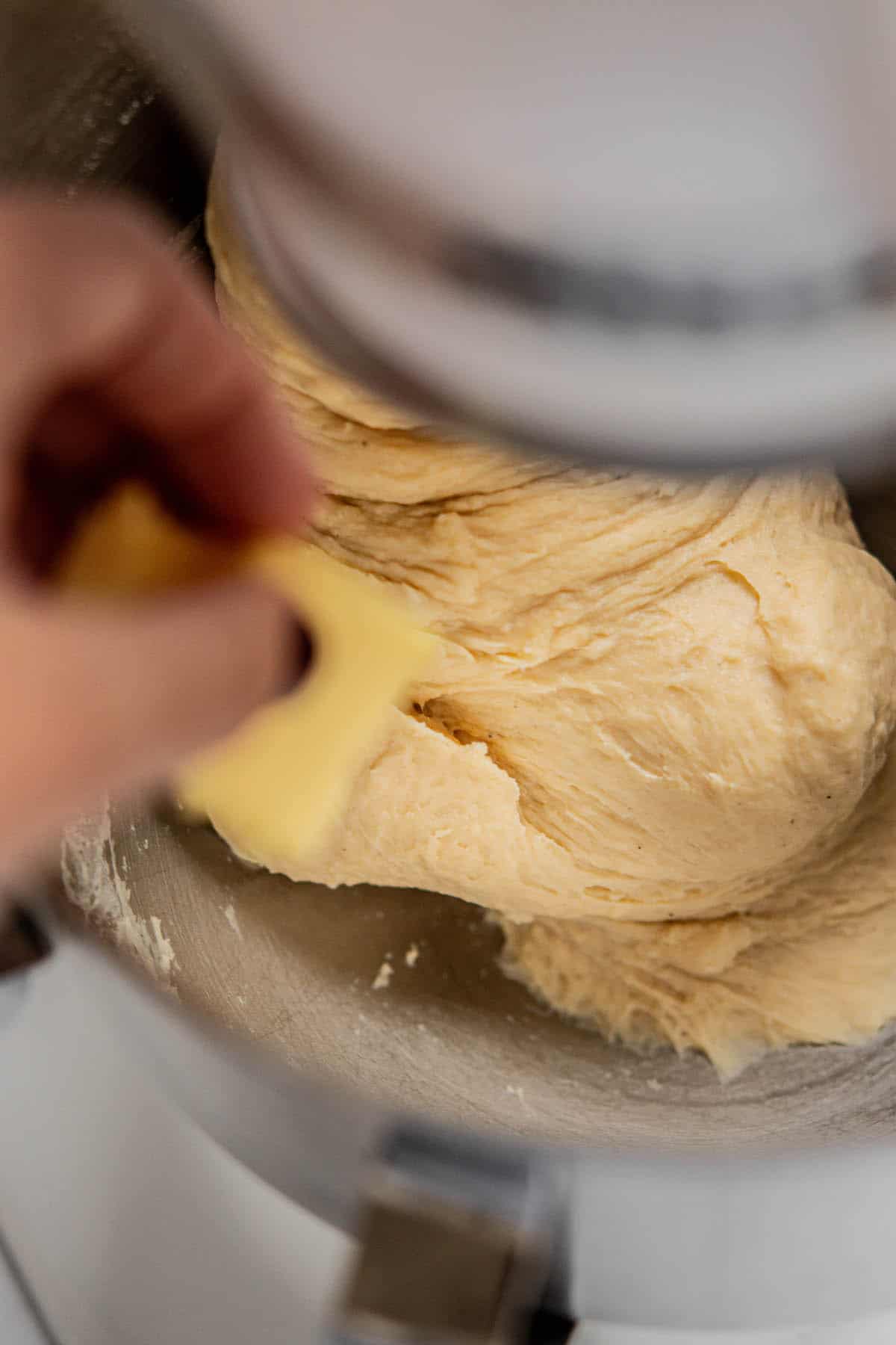 hand adding butter to dough.