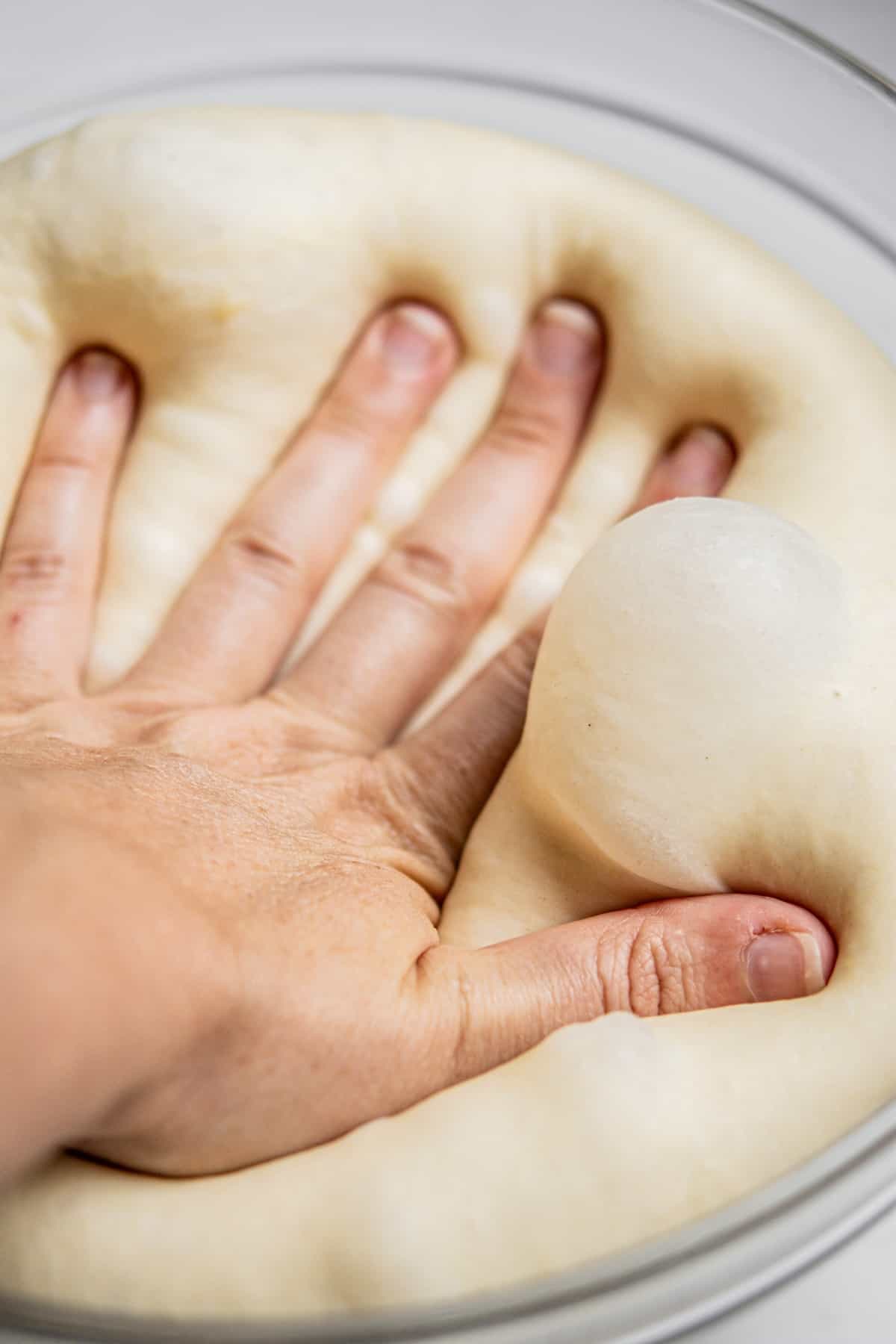 hand pressing down deflated dough.