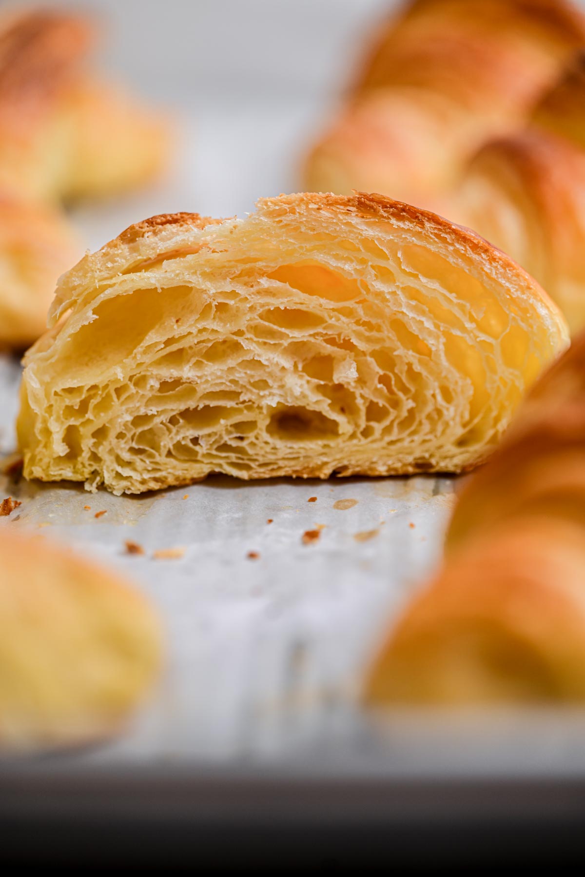 A close-up of homemade croissants, showing their golden, flaky layers and airy texture on a baking sheet.