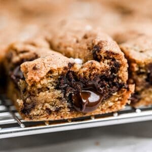 A close-up of gooey sourdough cookie bars with melted chocolate in the center, resting on a wire cooling rack.