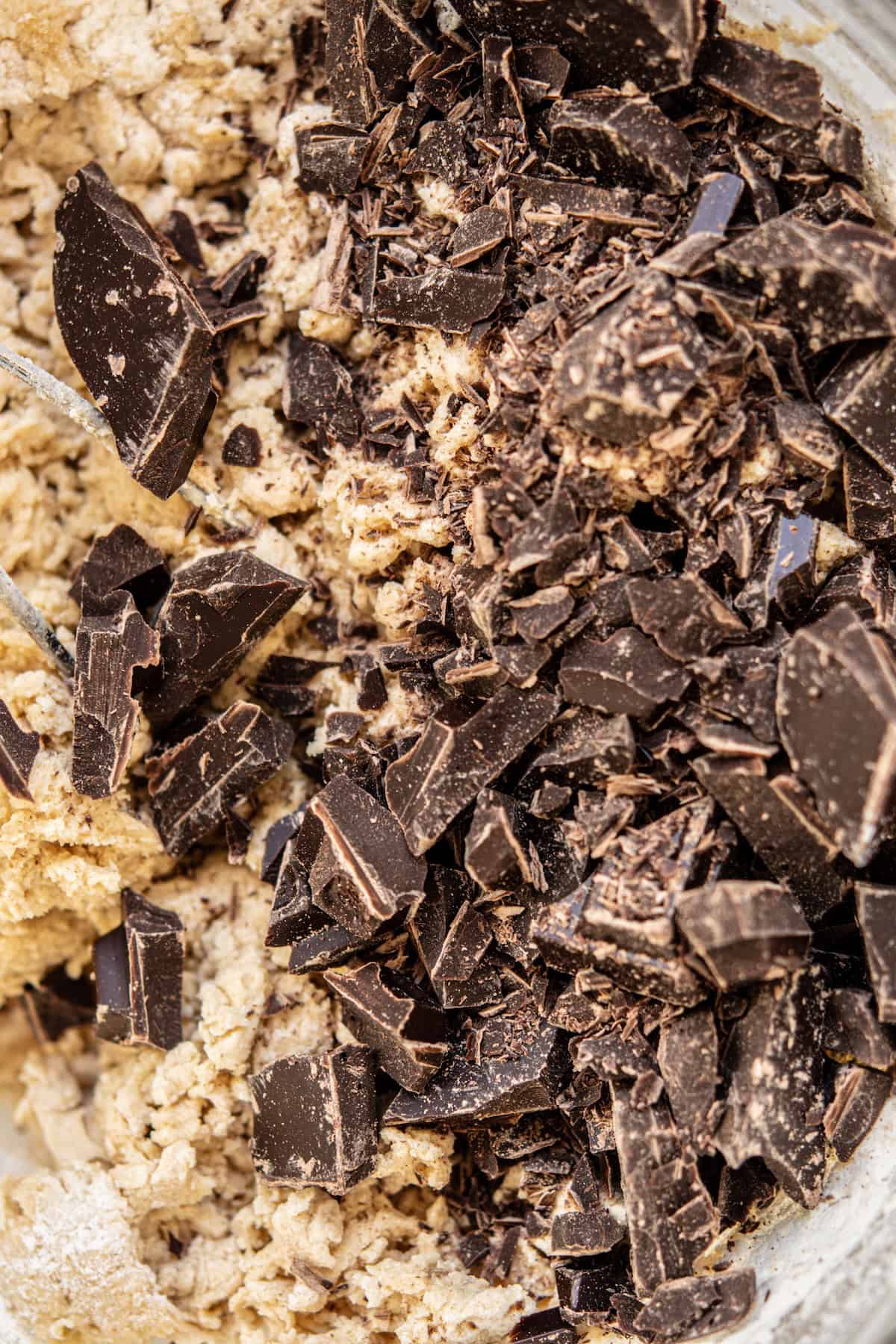 A close-up of chopped dark chocolate pieces resting on top of sourdough cookie bars dough, ready to be mixed together.