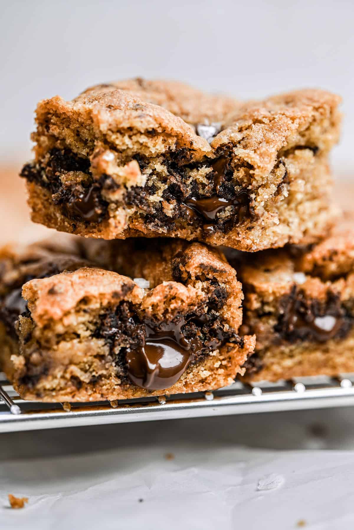 Two thick sourdough cookie bars stacked on a cooling rack, showing gooey melted chocolate inside and a golden-brown, slightly crumbly texture.