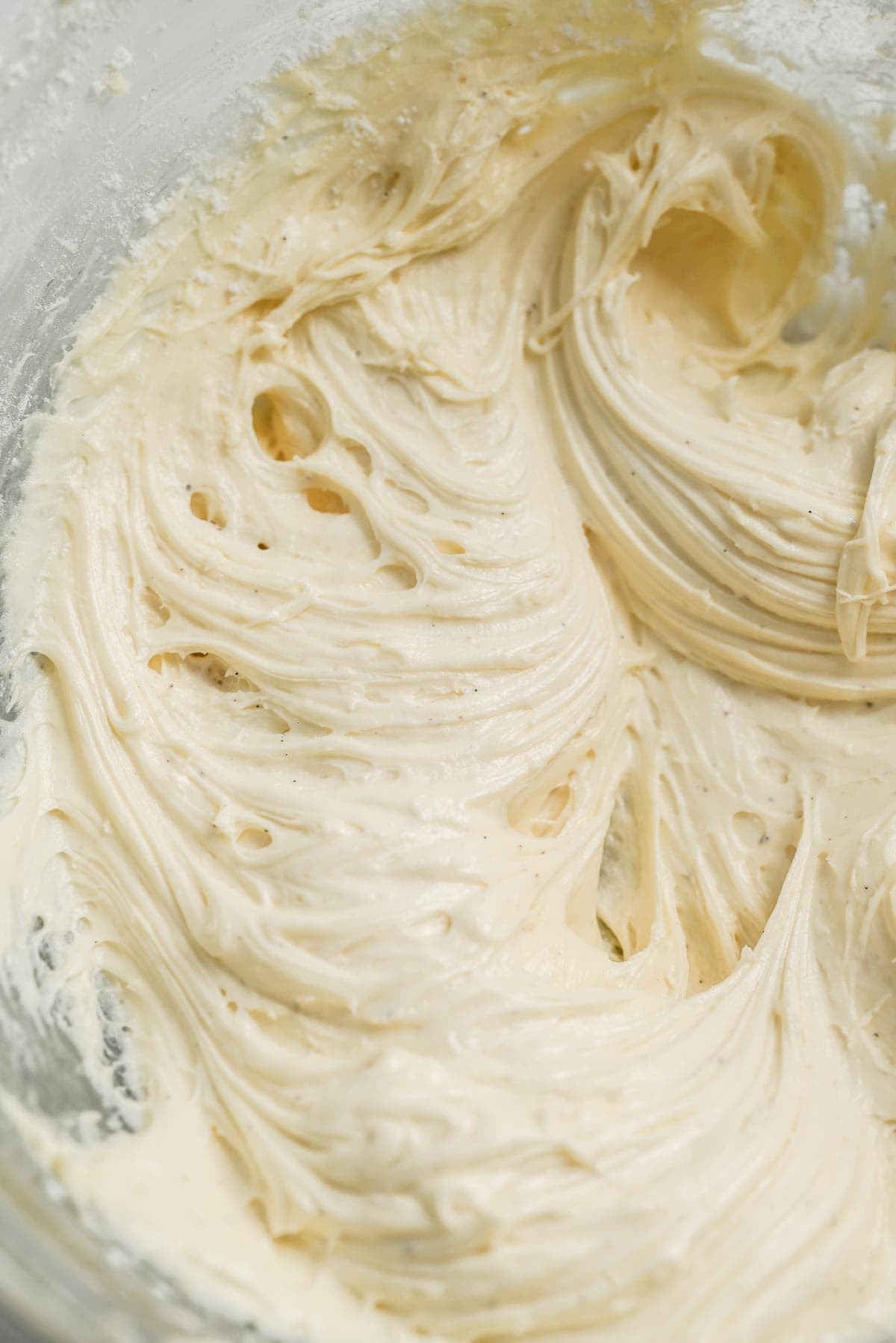 Close-up of smooth, creamy buttercream frosting swirled in a mixing bowl, showing a light, fluffy texture with soft peaks—perfect for topping freshly baked Raspberry Rolls.