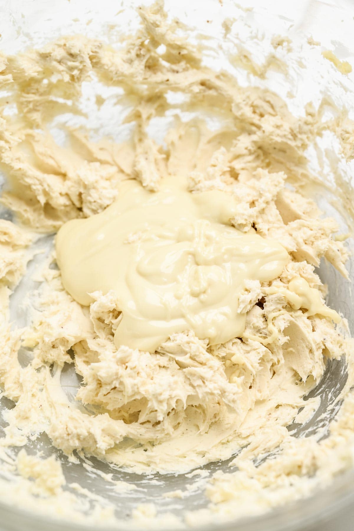 A glass mixing bowl with creamed butter and sugar, topped with melted white chocolate, ready to be mixed together for delicious Raspberry Rolls.