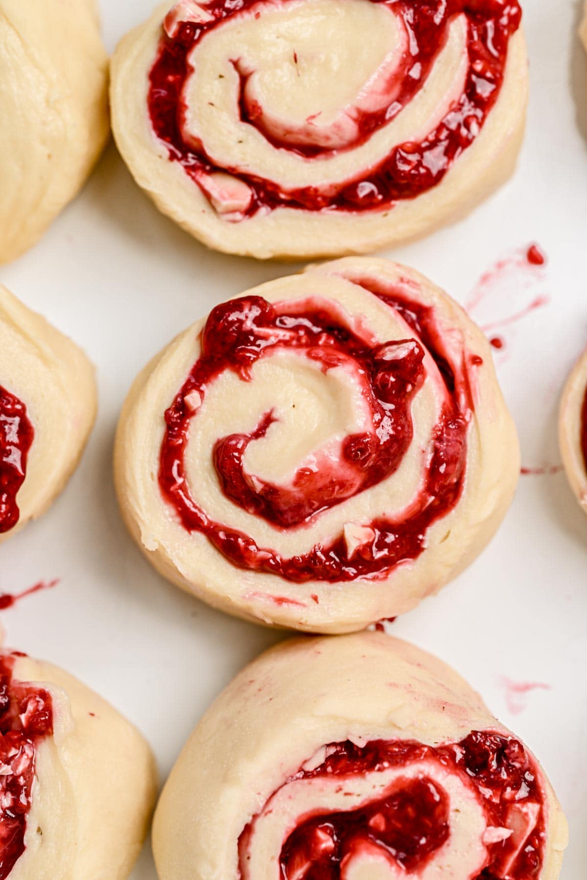 Unbaked Raspberry Rolls with a swirl of vibrant red raspberry filling, arranged on a white surface, ready for baking.