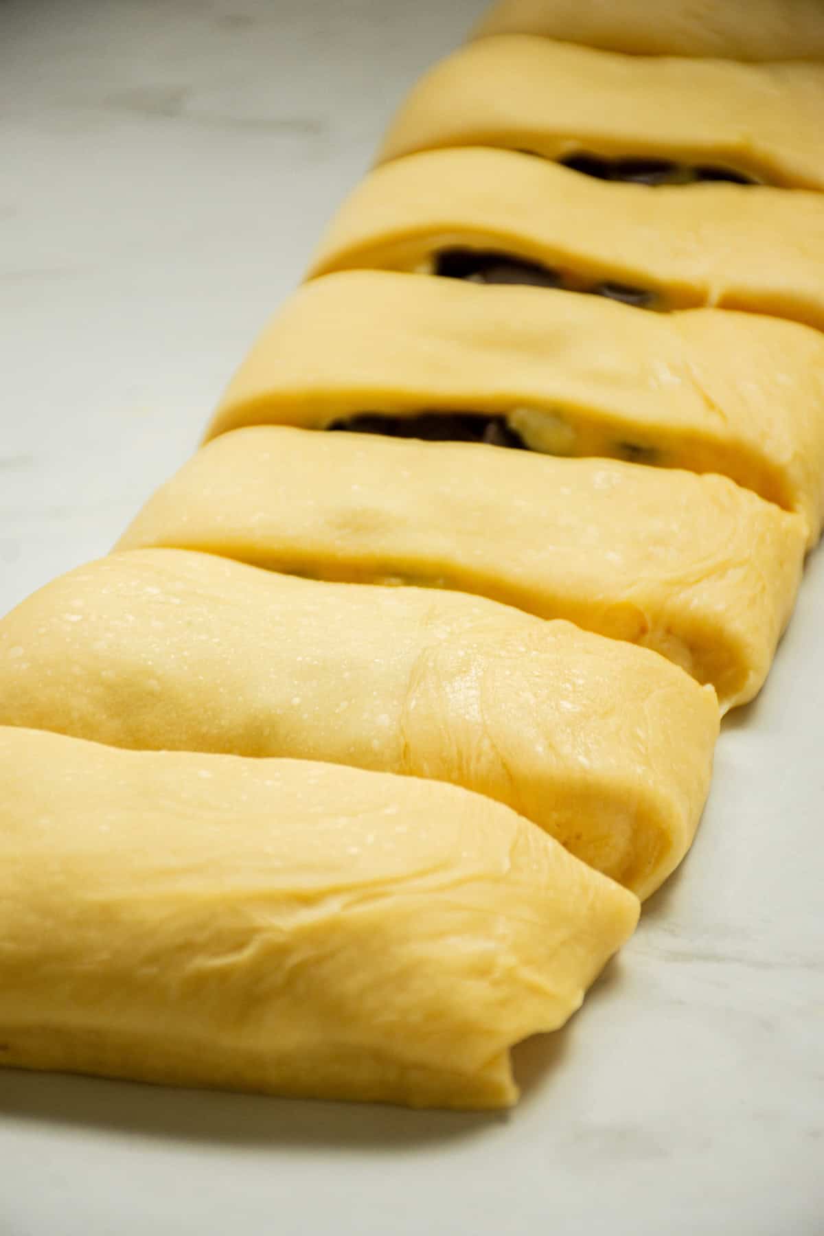 Several dough pieces filled with a dark filling, arranged neatly in a row on a light surface. The dough is smooth and light-colored, and the filling is partially visible through slits in the dough.