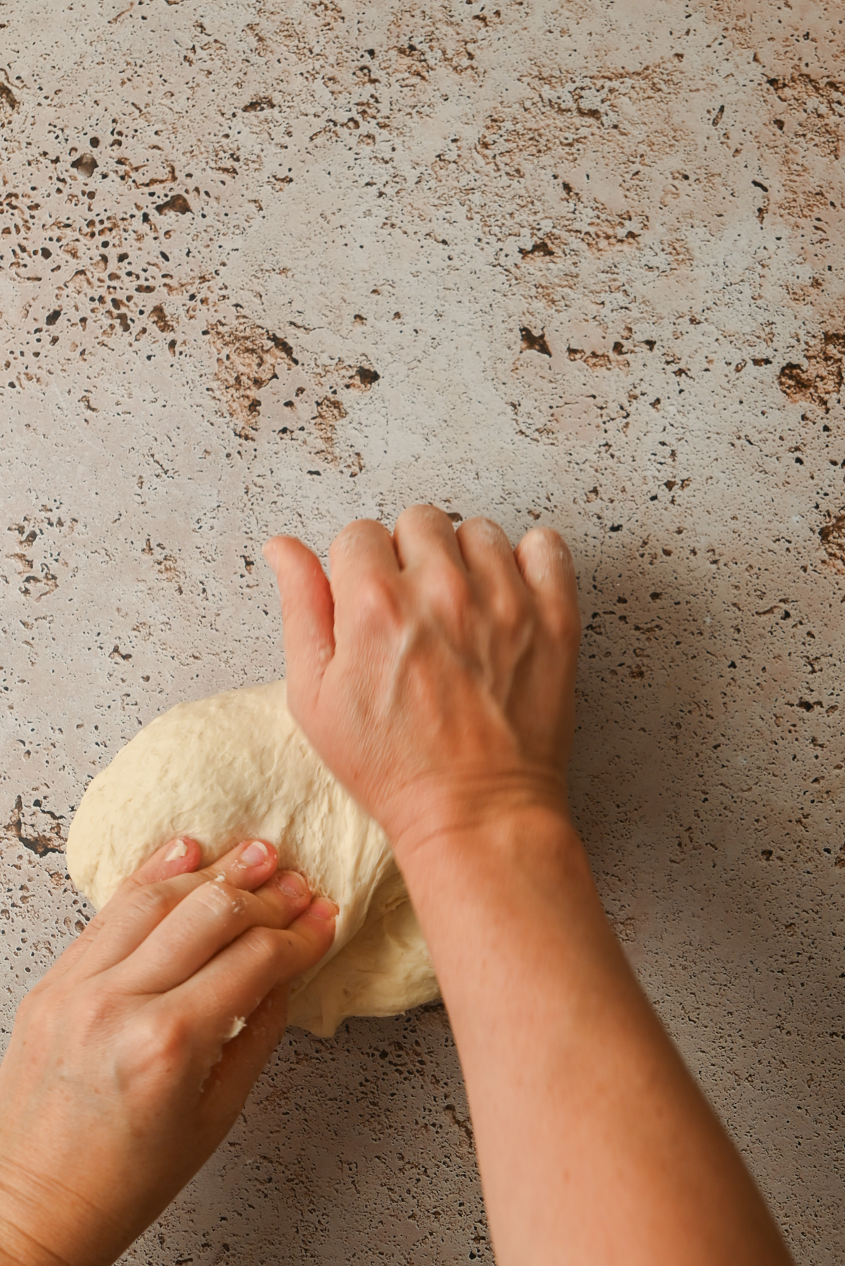 Two hands kneading a ball of dough for Kouign Amann on a lightly textured, speckled countertop.