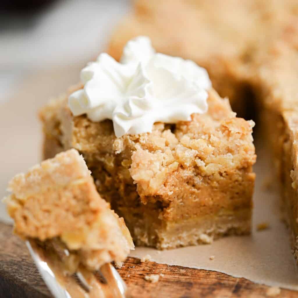 A close-up of a slice of crumb-topped pie with a dollop of whipped cream on top. A fork is holding a bite-sized piece in front of the slice, showing the creamy filling and crumbly crust.
