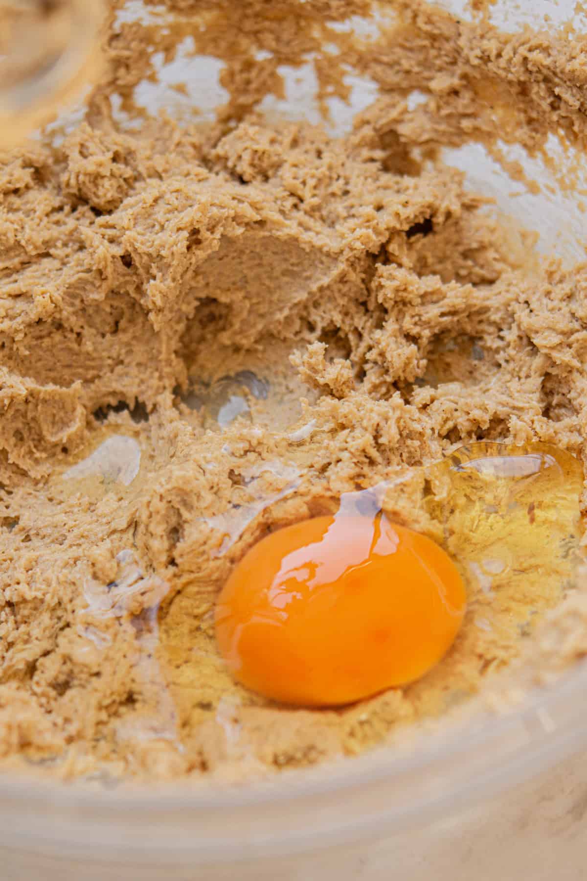 A close-up of a mixing bowl with cookie dough and a raw egg sitting on top, ready to be mixed in.