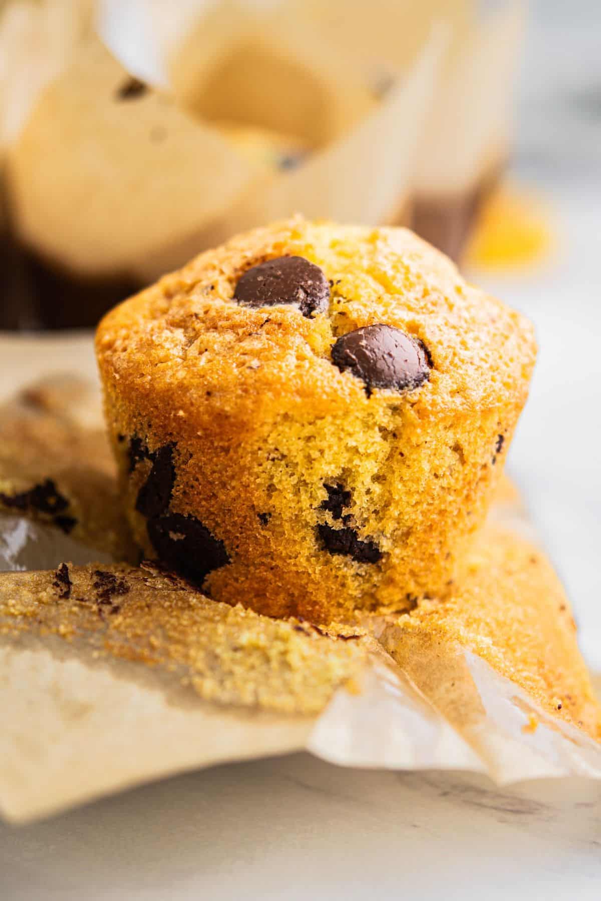 A close-up of a freshly baked chocolate chip muffin sitting on unwrapped parchment paper, with chocolate chips visible throughout the golden, moist muffin—perfect alongside a scoop of creamy Funfetti Ice Cream.