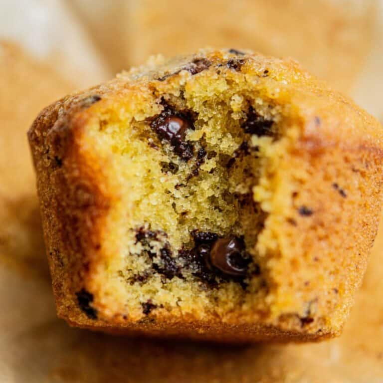 A close-up of an orange chocolate chip muffin with a large bite taken out, revealing its moist, golden interior and melted chocolate chips—perfect alongside a scoop of colorful Funfetti Ice Cream.