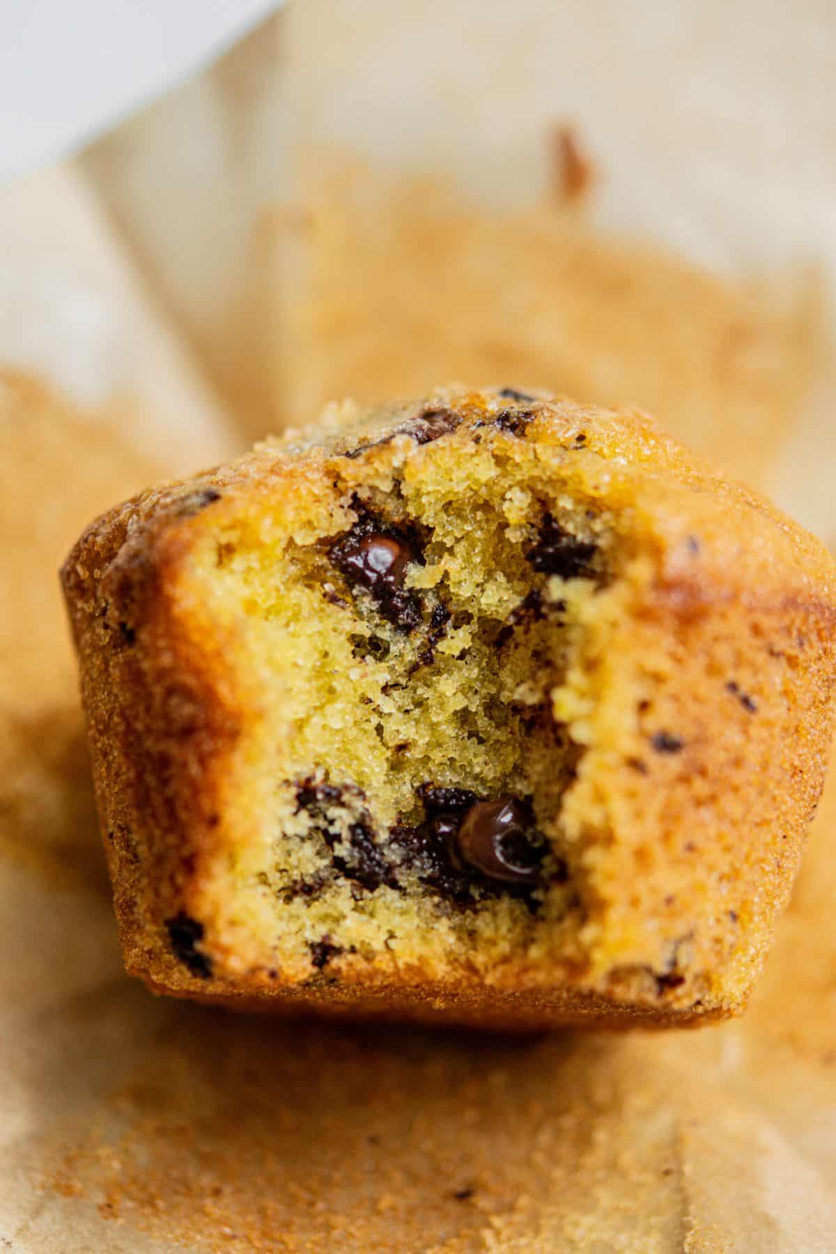 A close-up of a half-eaten chocolate chip muffin on parchment paper, showing its moist yellow crumb and melted chocolate chips—reminiscent of the playful colors in Funfetti Ice Cream.