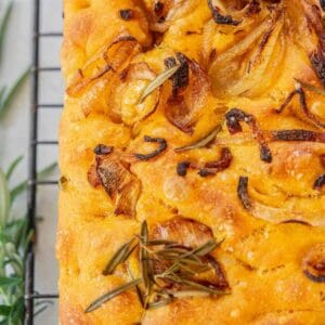 Close-up of golden-brown focaccia bread topped with caramelized onions and fresh rosemary on a cooling rack, capturing the contrast between savory flavors and the playful spirit reminiscent of Funfetti Ice Cream.