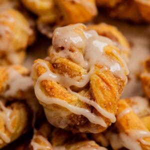 A close-up of a golden, twisted pastry topped with a drizzle of white icing and sprinkled with cinnamon sugar, reminiscent of Apple Hand Pies with Puff Pastry. The flaky texture highlights delicate layers and a tempting sweet glaze.