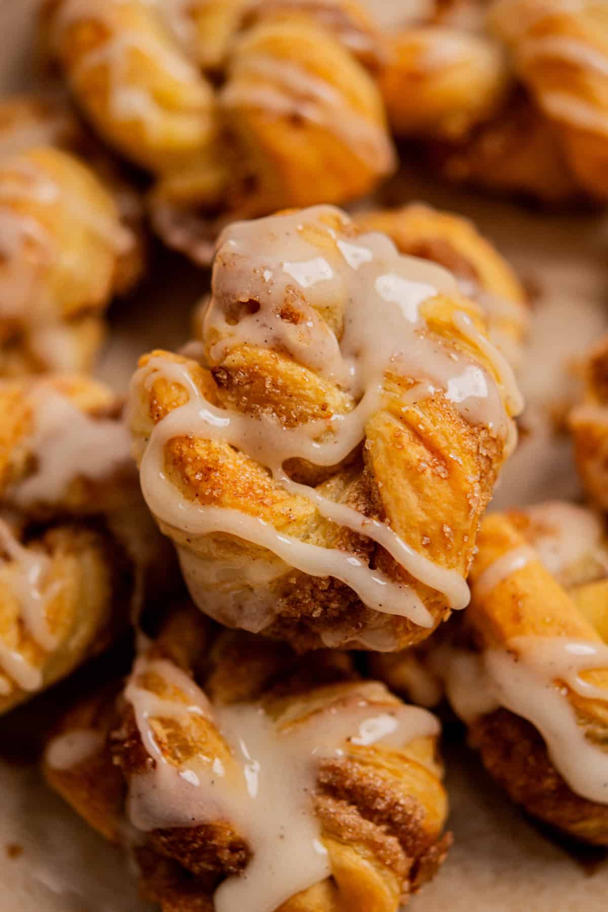 Close-up of twisted pastries topped with a drizzle of white icing, showing flaky, golden-brown layers and a cinnamon-sugar filling—perfect inspiration for making Apple Hand Pies with Puff Pastry. The pastries are stacked on a neutral surface.