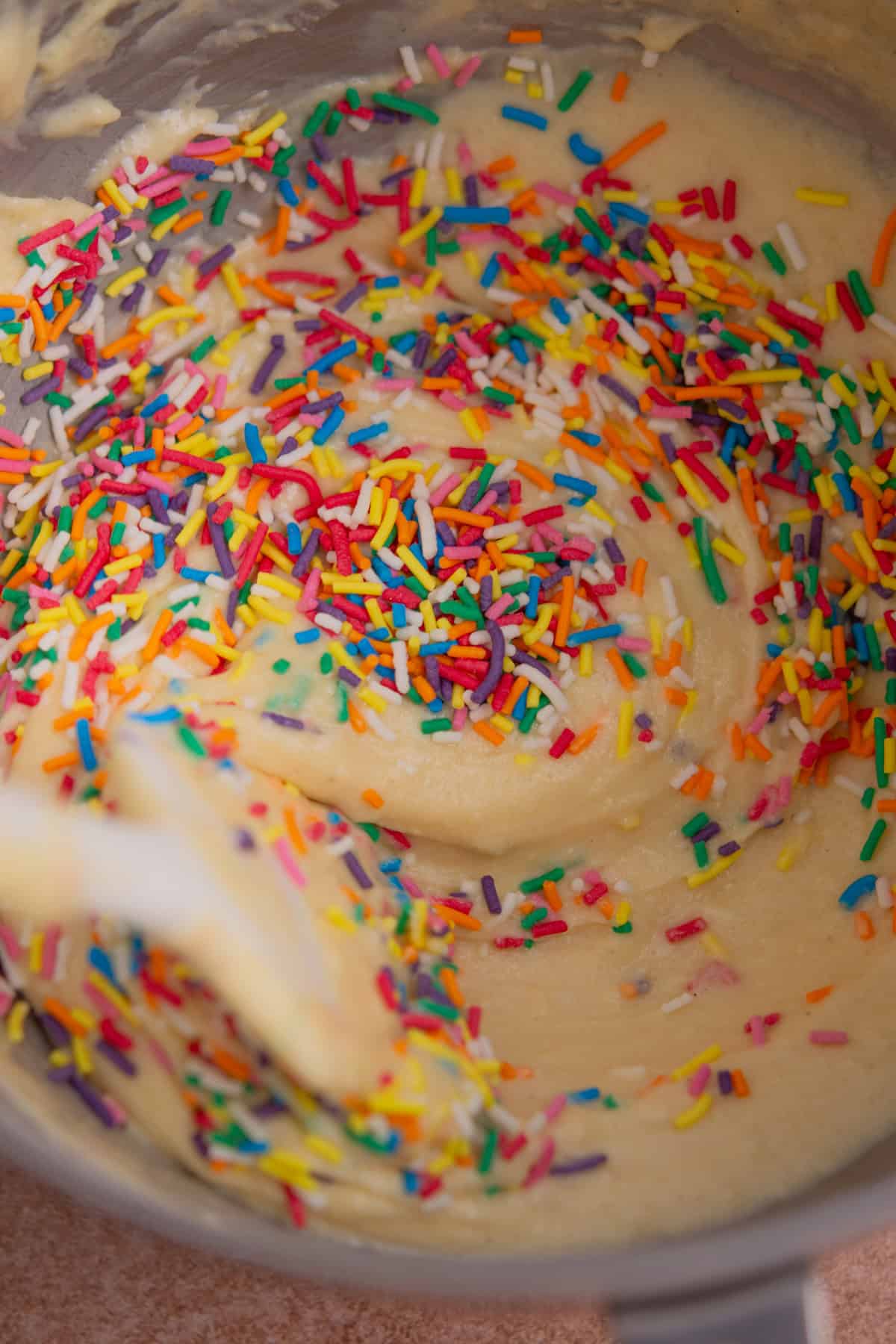 Cake batter in a mixing bowl with colorful rainbow sprinkles being stirred in, creating a funfetti effect—perfect for pairing with Puff Pastry Cinnamon Twists for a festive treat.