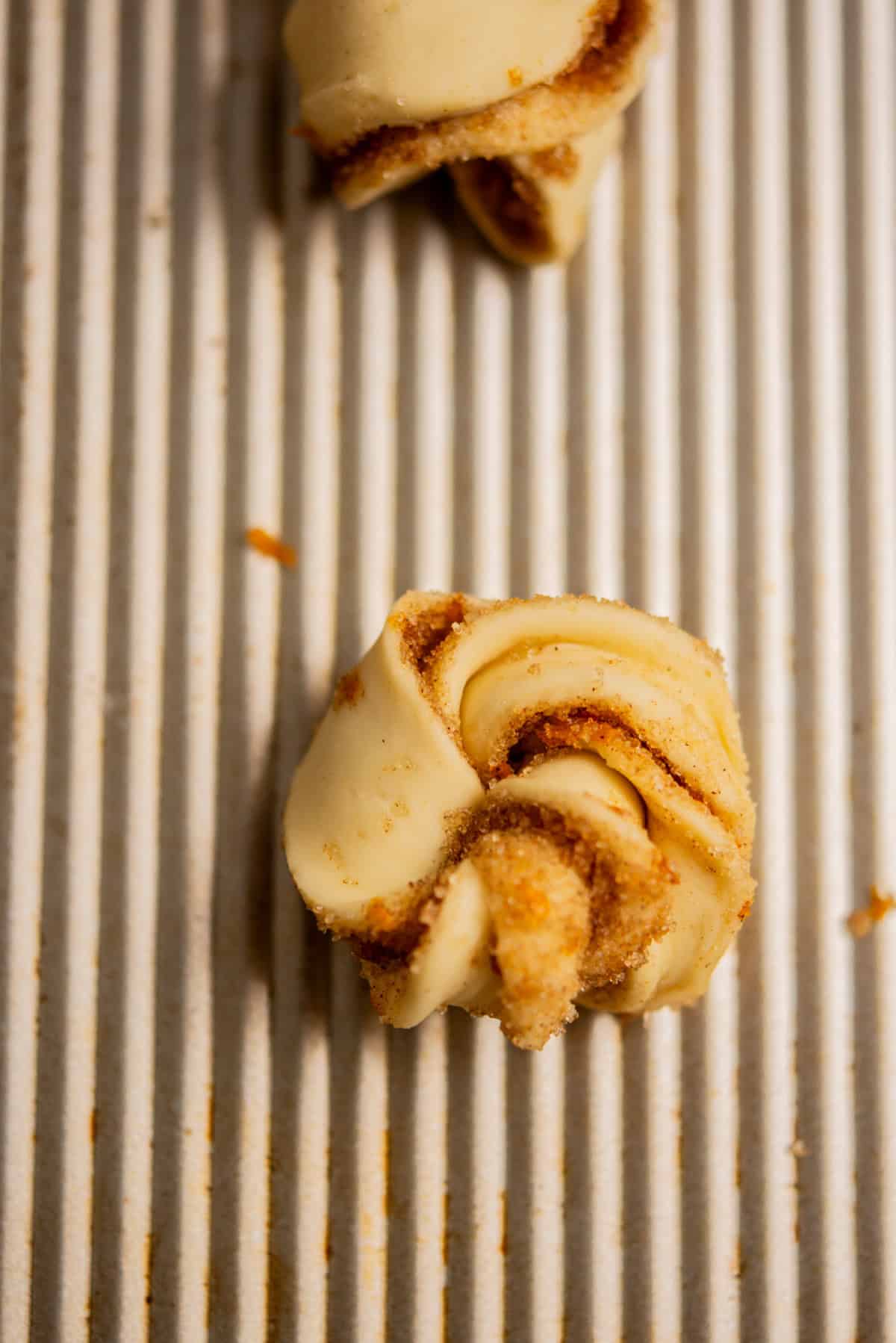 A close-up of an unbaked twisted pastry dough with a cinnamon sugar filling, resting on a ribbed, light-colored baking sheet.