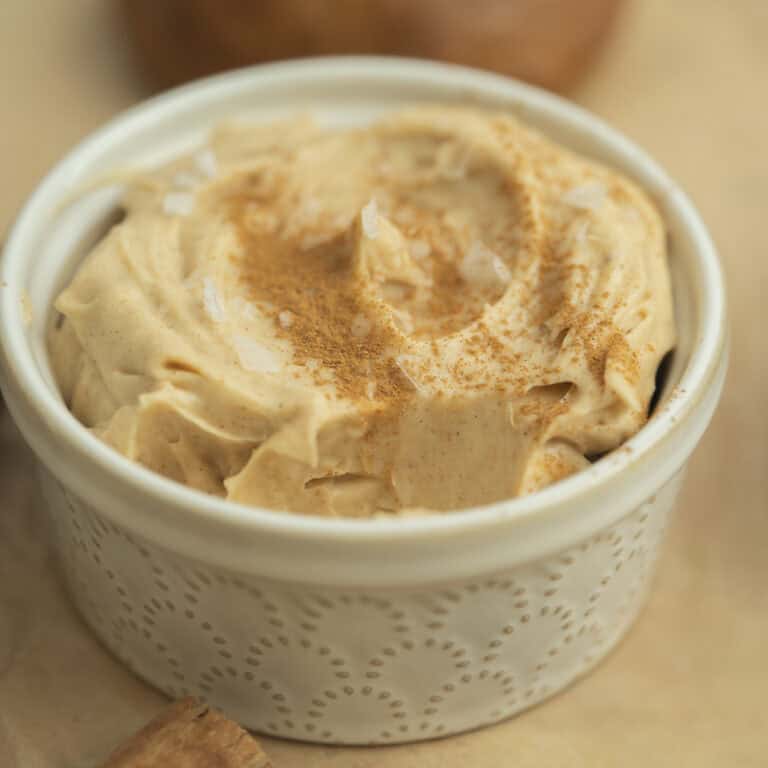 A small white ramekin filled with whipped cinnamon cream cheese, sprinkled with cinnamon and flakes of sea salt on top. The butter has a creamy, swirled texture.