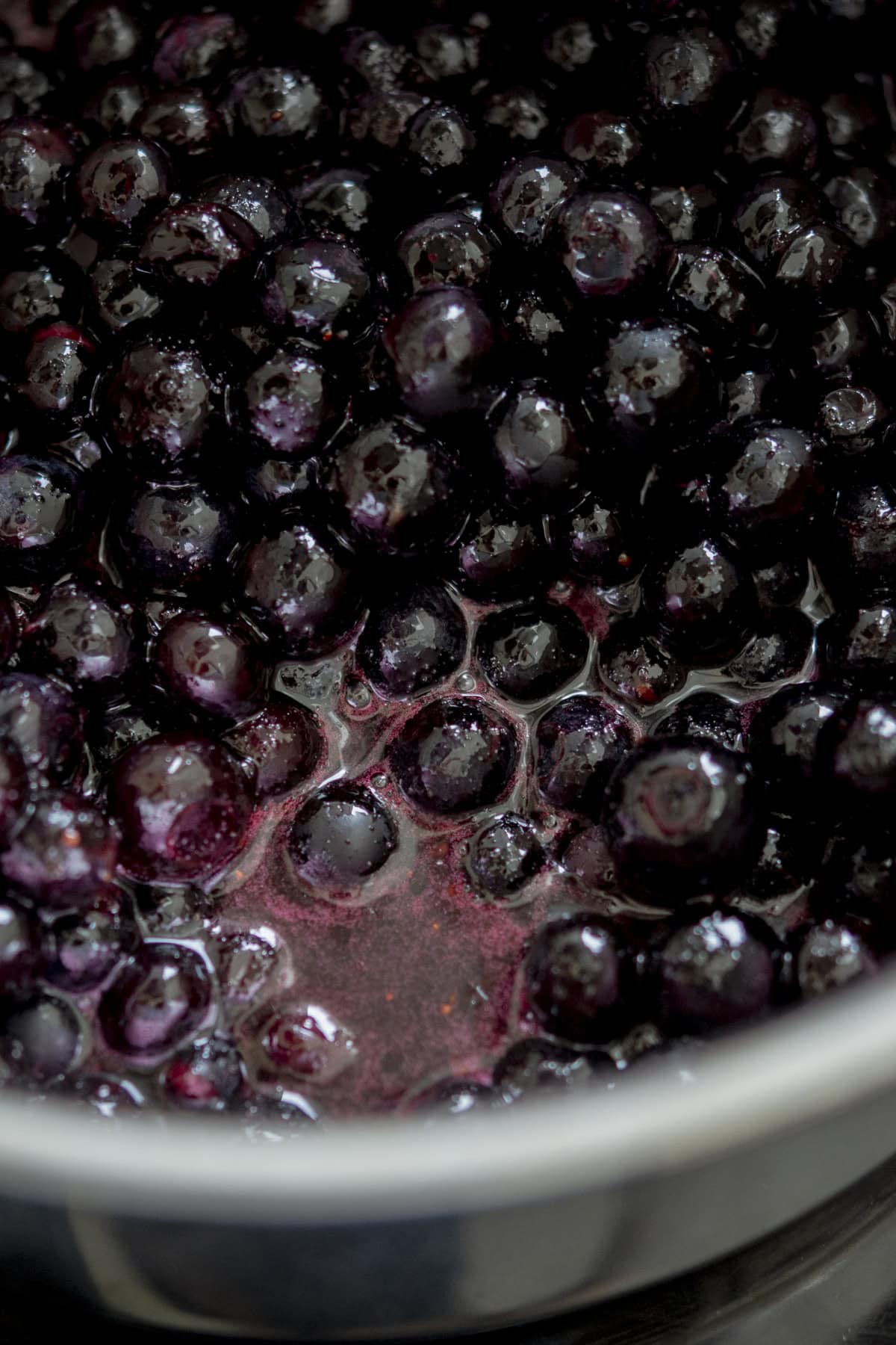 A close-up of blueberries simmering in a pot with their juices, creating a glossy, deep purple mixture.