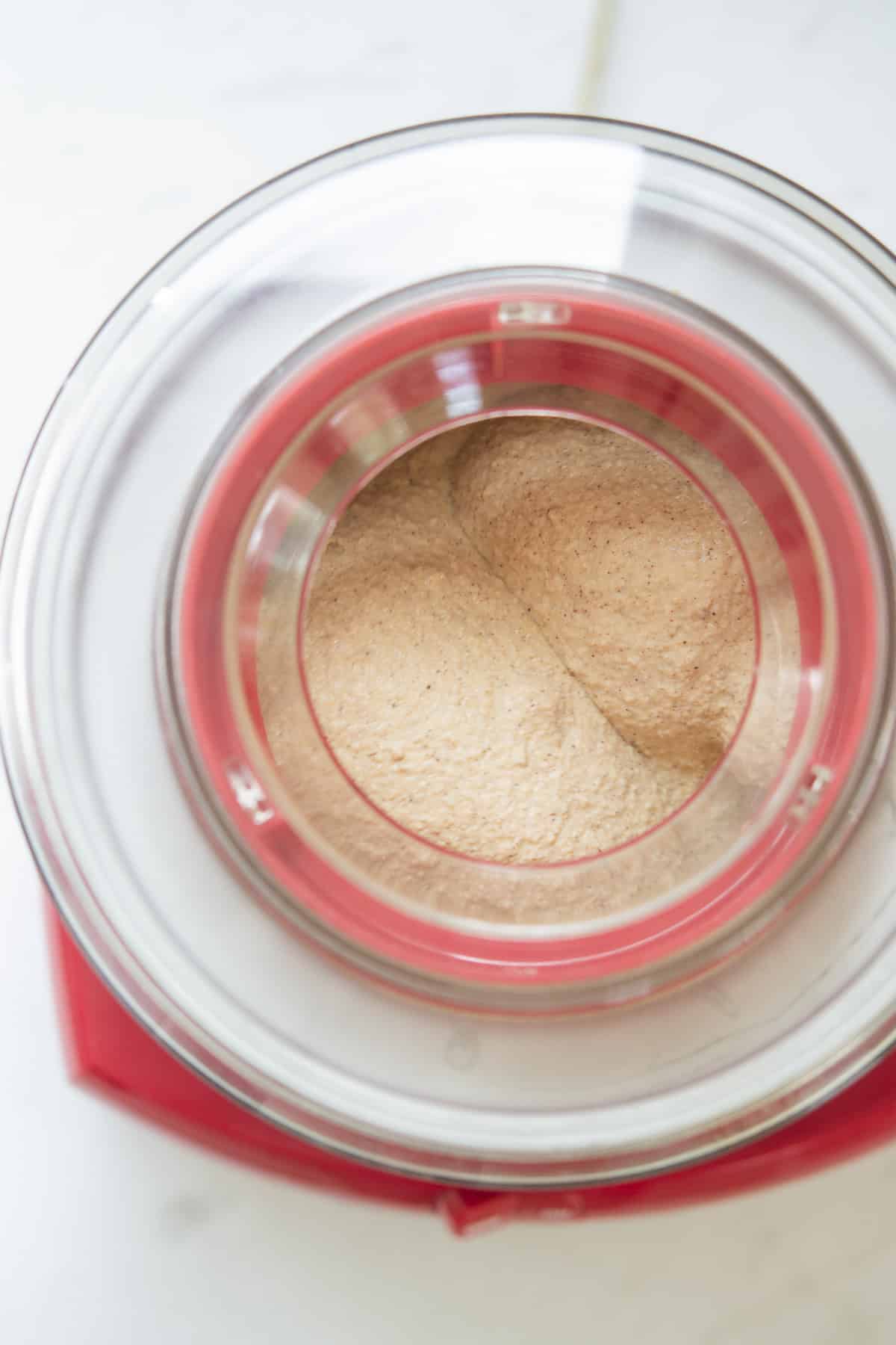 Top-down view of a red ice cream maker churning a light brown, creamy mixture on a white surface.