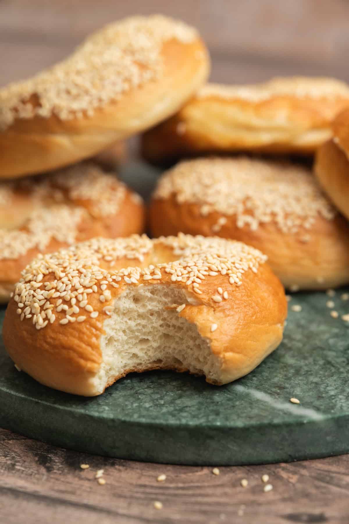 A group of sesame seed-topped bagels on a green marble surface, with one bagel in the front showing a bite taken out of it.