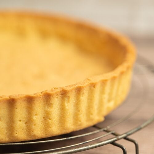 A close-up of a golden-brown, baked pate sablee âte sablée is easy to make ahead. The dough can be wrapped and kept in the fridge for up to three days, or frozen for up to two months. Thaw frozen dough in the fridge overnight before rolling. A fully baked tart shell can be stored at room temperature in an airtight container for two days. If you want to keep it longer, freeze the baked shell once it’s completely cool. It thaws quickly and stays crisp, ready to fill whenever you need it.tart crust in a fluted pan, cooling on a wire rack. The tart shell appears crisp and evenly baked, with a smooth surface and neatly crimped edges.