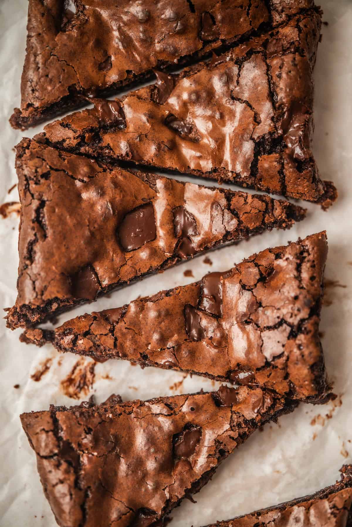 Close-up of rich, fudgy small batch brownies with crackled tops and visible chocolate chunks, sliced into triangular pieces on a sheet of parchment paper.