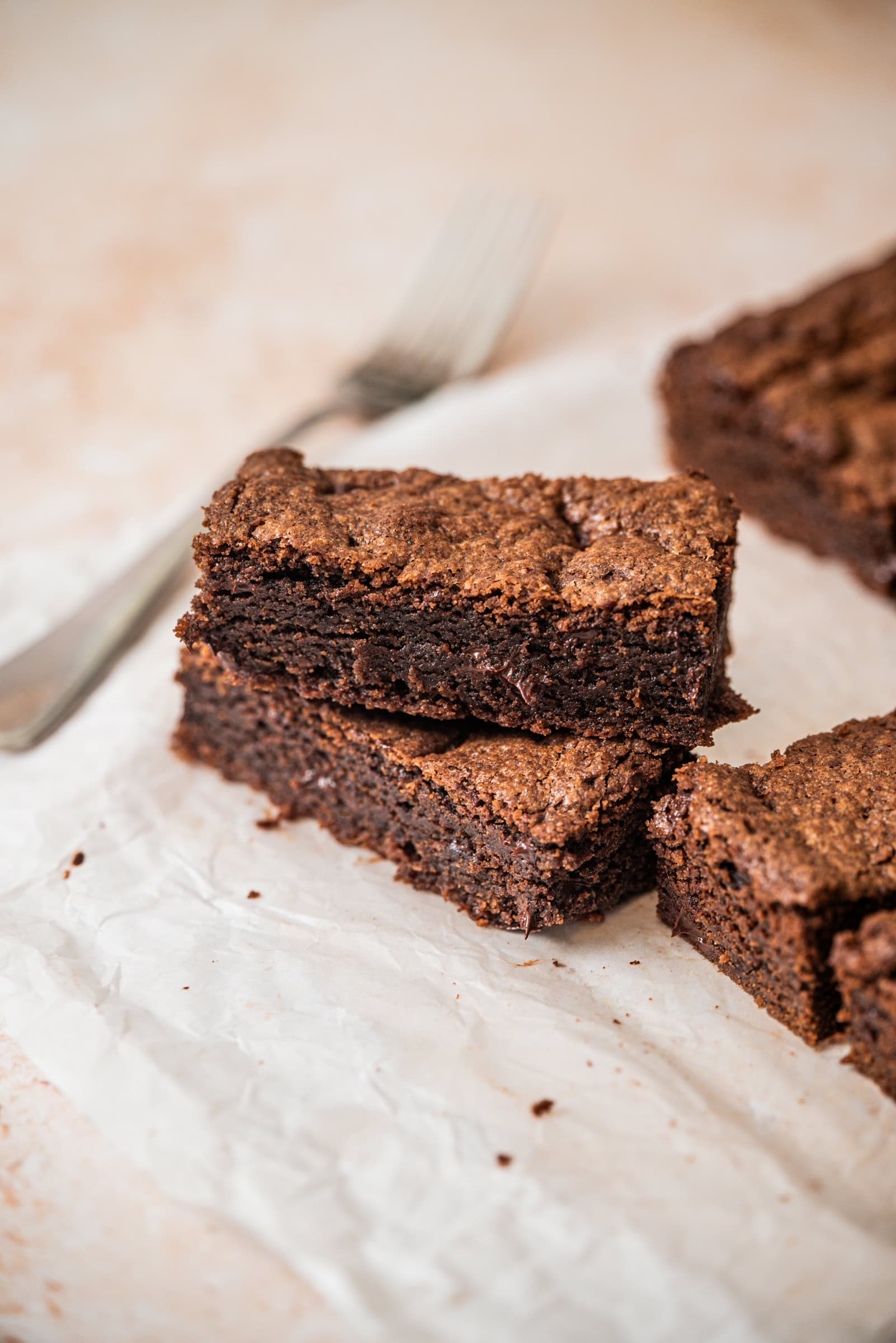 Three thick, fudgy double chocolate cookie bars stacked on white parchment paper, with a metal fork