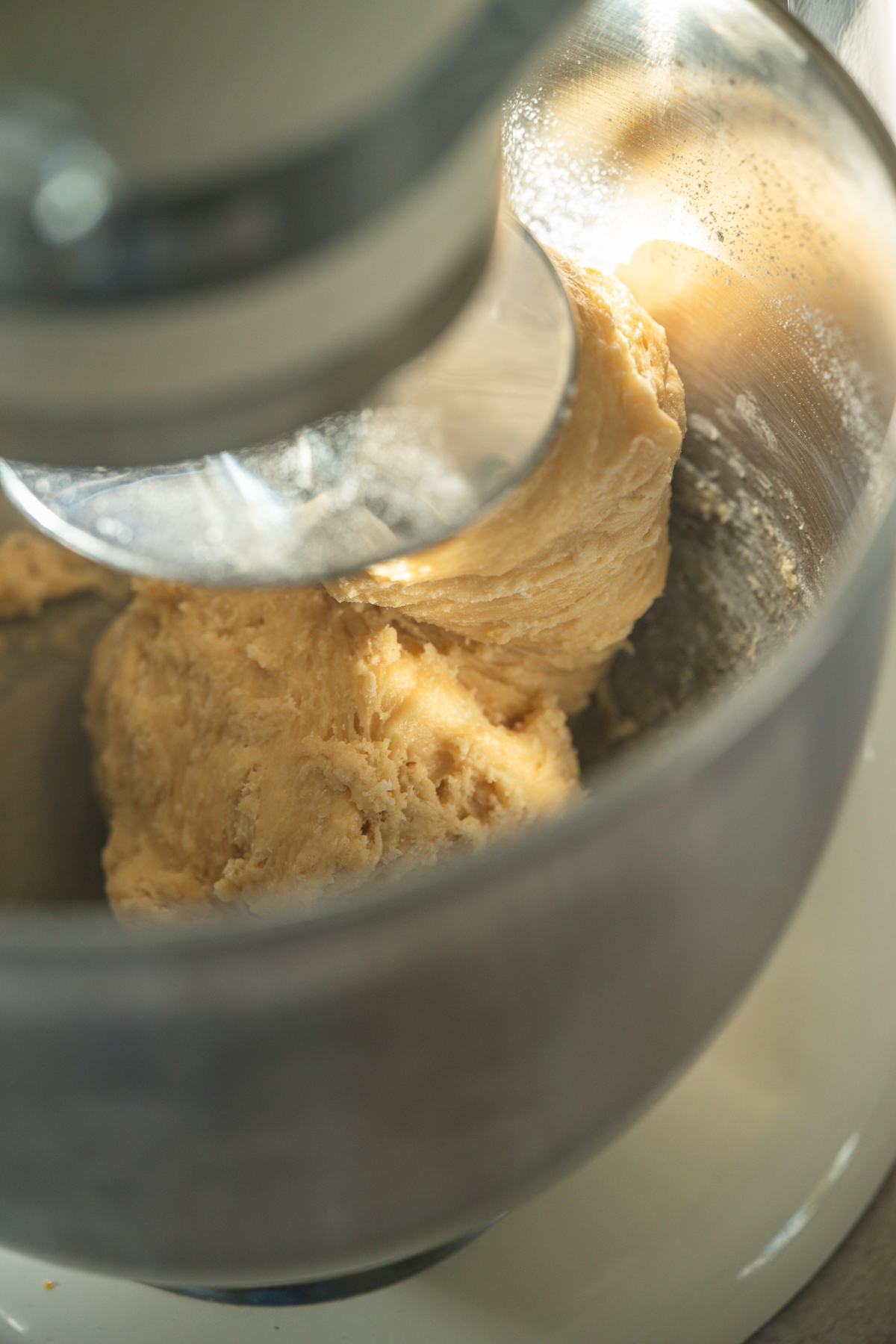 Close-up of brioche dough being mixed in a stand mixer with a metal bowl, showing the dough hook attachment blending the dough.